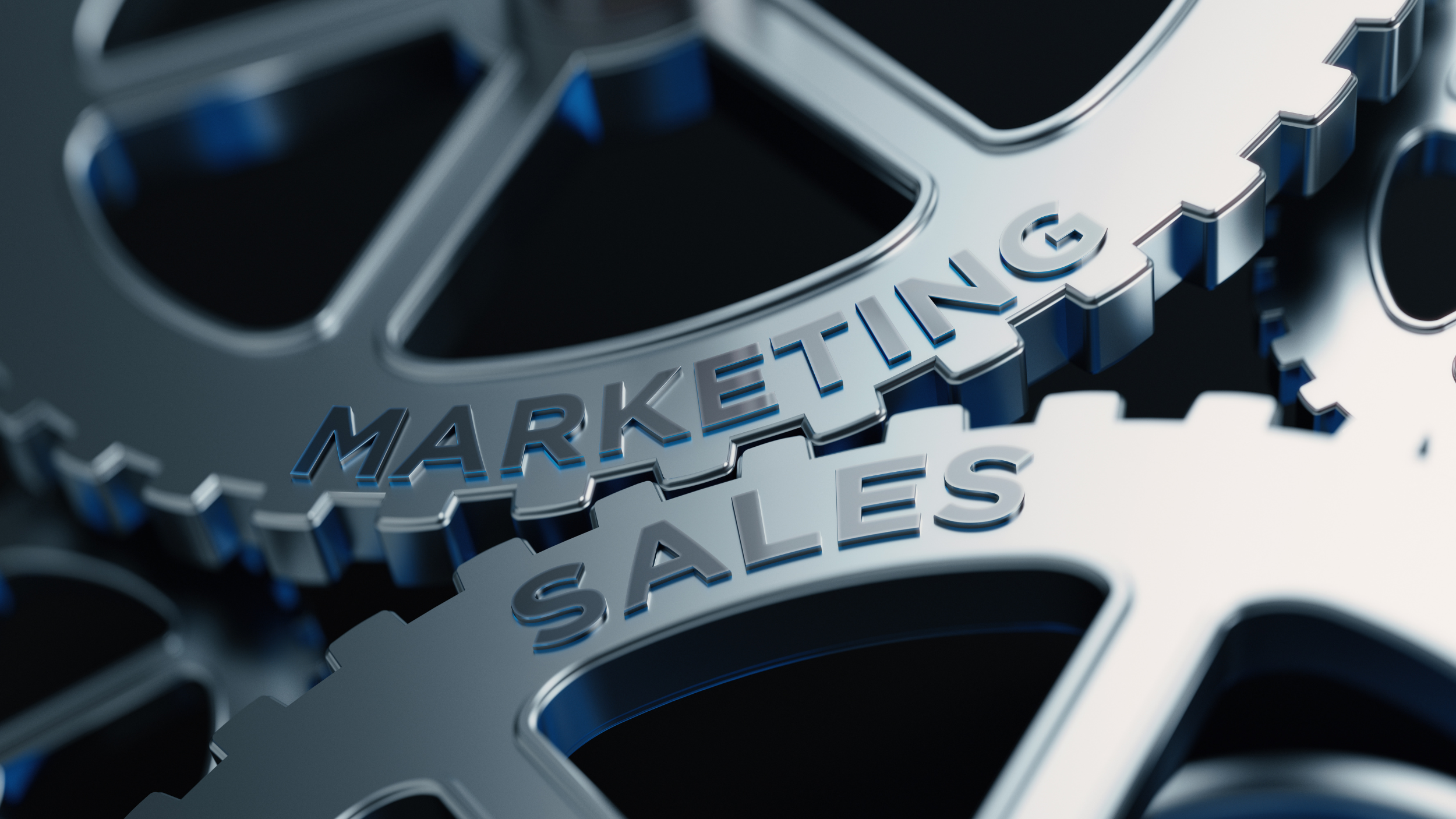 Close-up of metallic gears with the words "MARKETING" and "SALES" engraved on the gears.