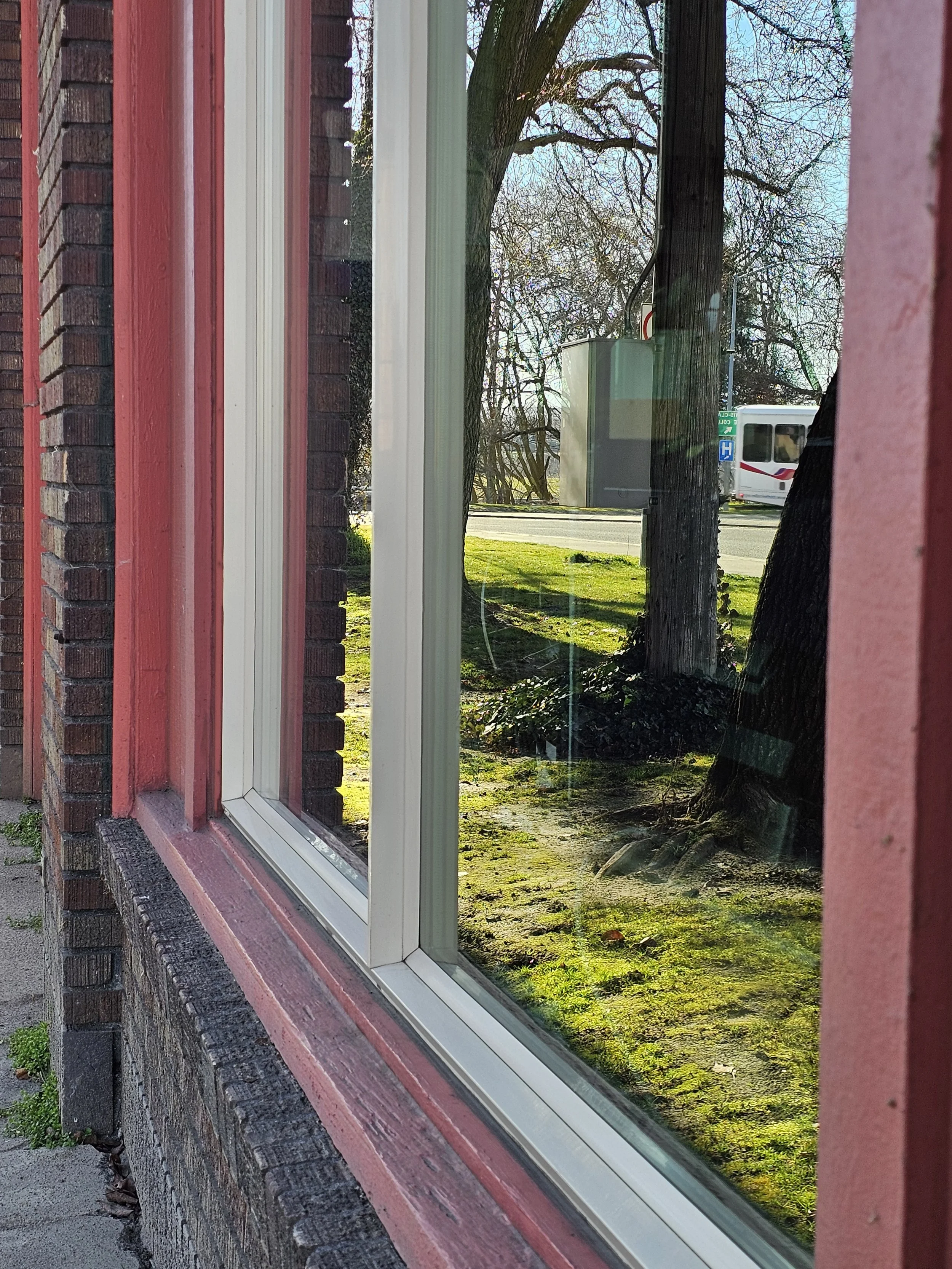 Looking through a window reflects trees, grass, and a bus passing by outside.