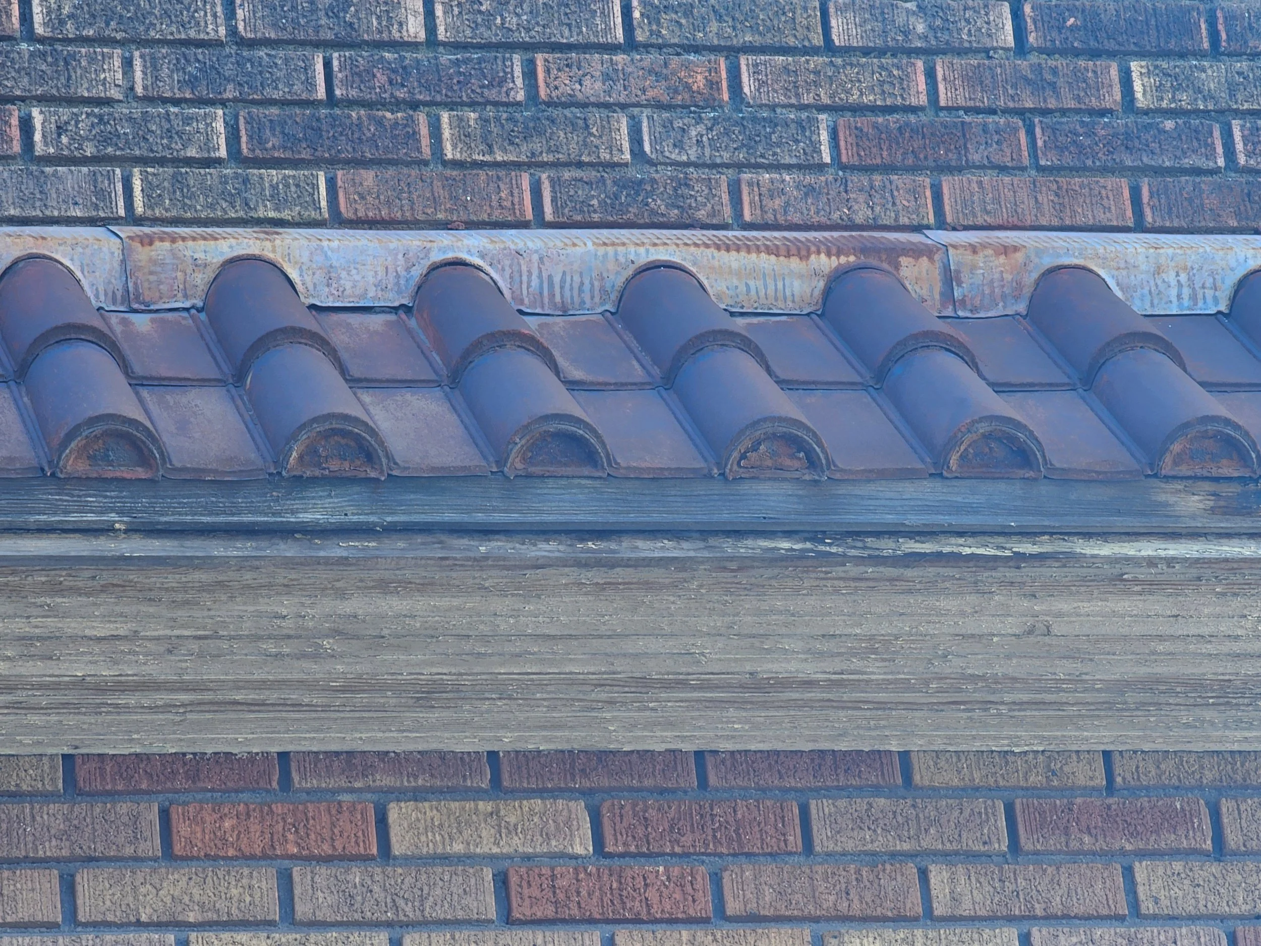 Close-up of a section of brick wall with a row of blue curved roof tiles and a weathered wooden beam below the tiles.