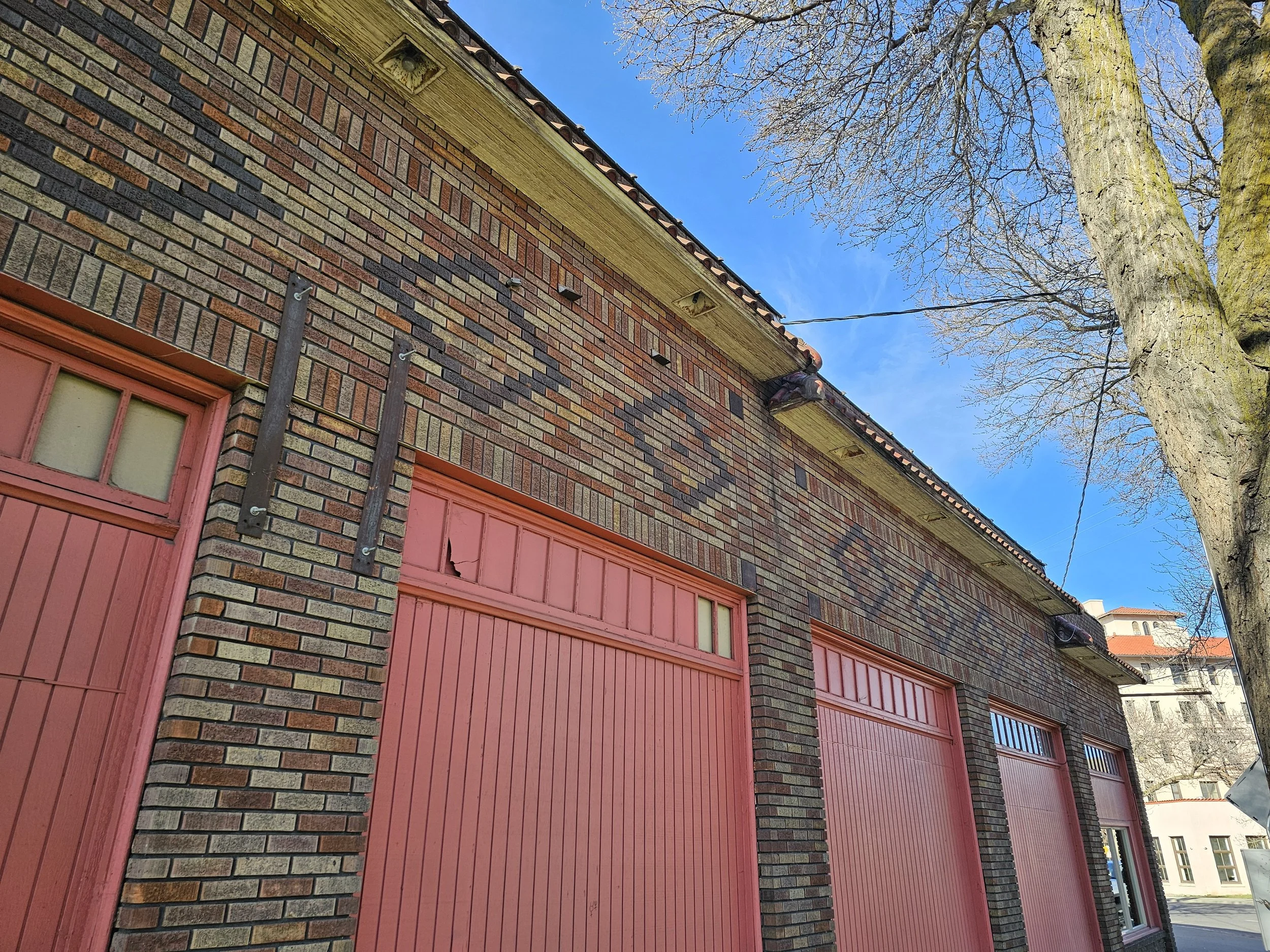 A brick building with pink garage doors and a large tree in front, clear blue sky overhead.