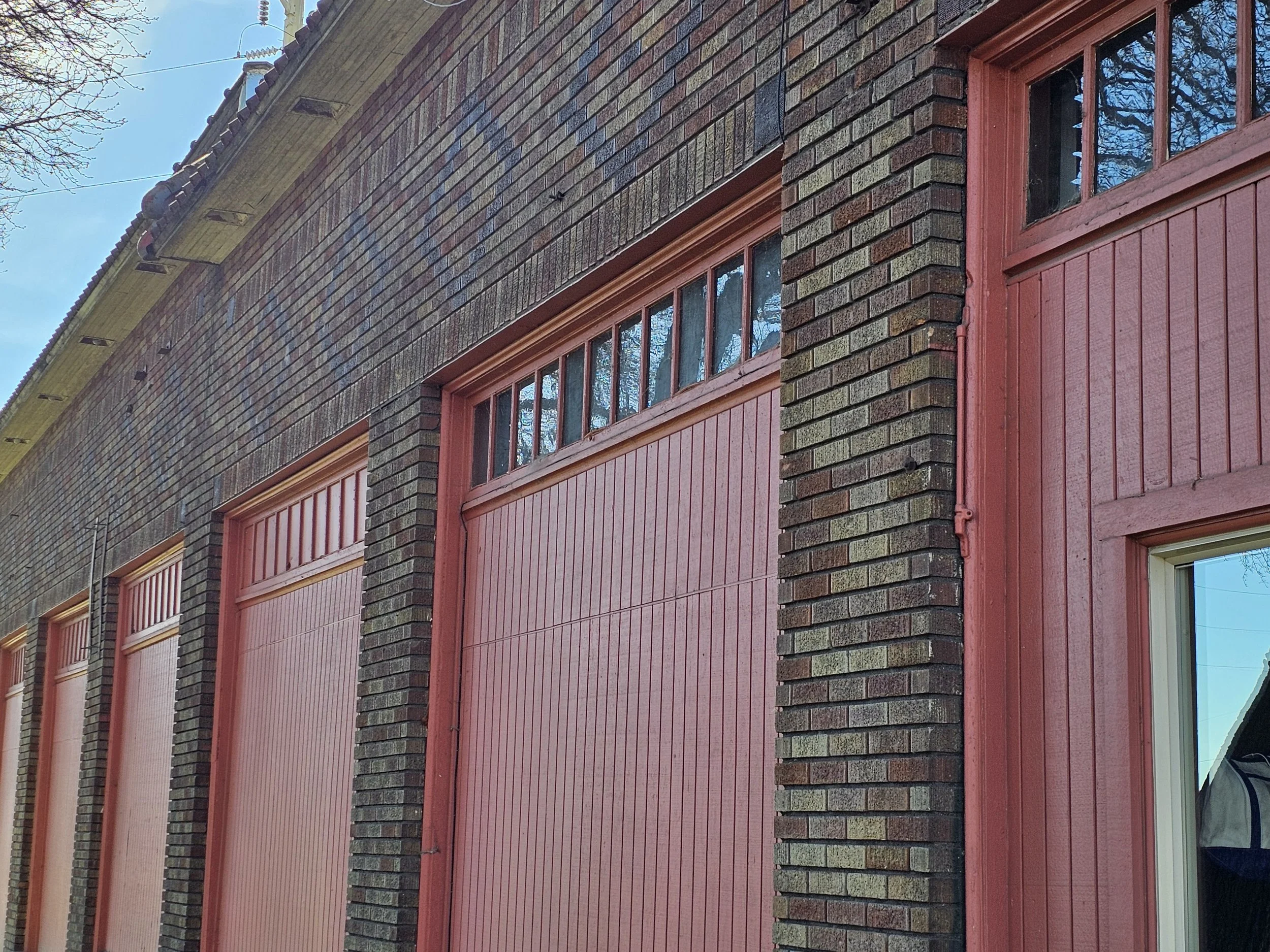 Close-up of a brick building with red garage doors and large windows at the top of each door.