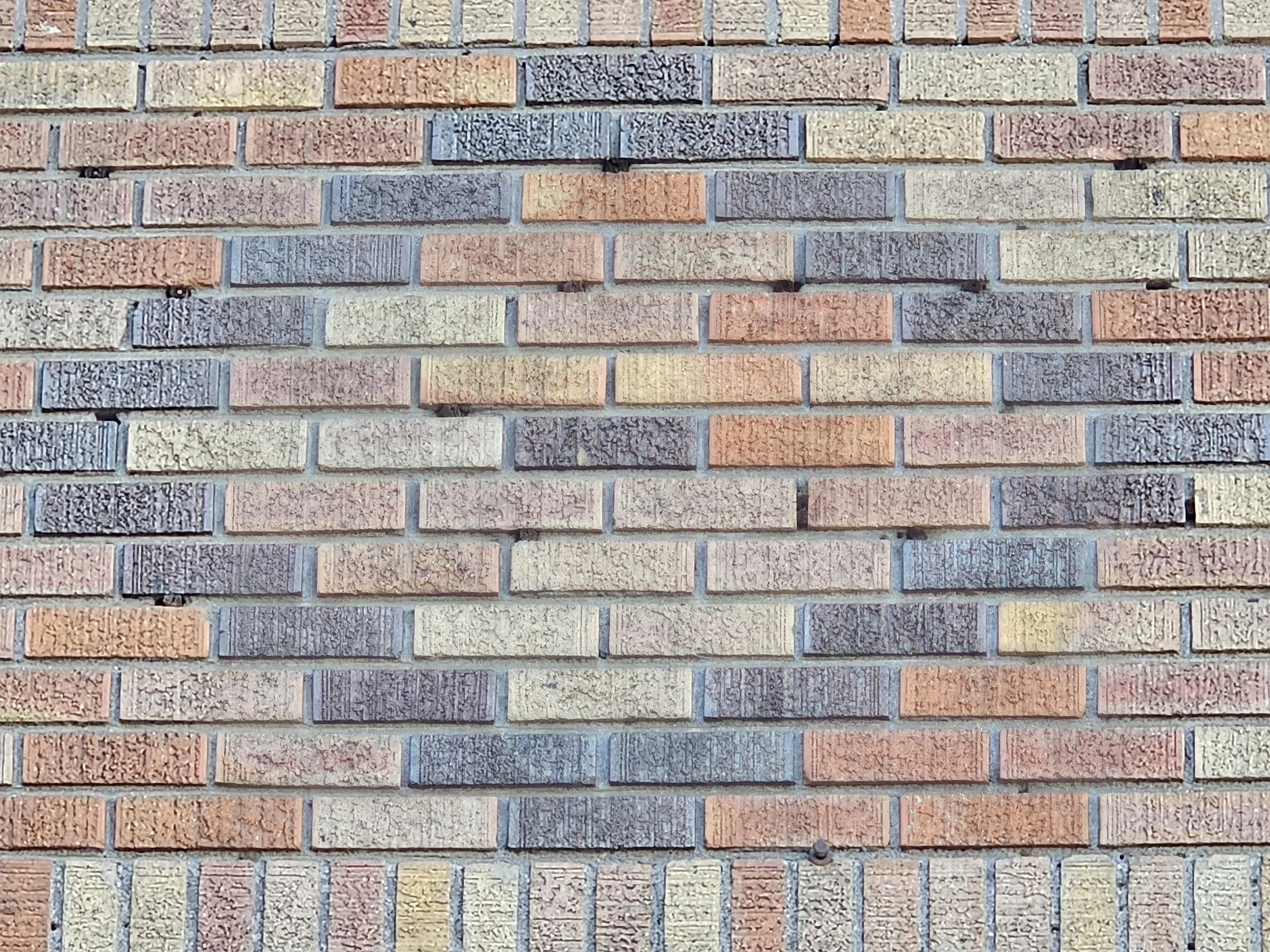 Close-up of a multicolored brick wall with red, beige, blue, and gray bricks aligned in horizontal rows.