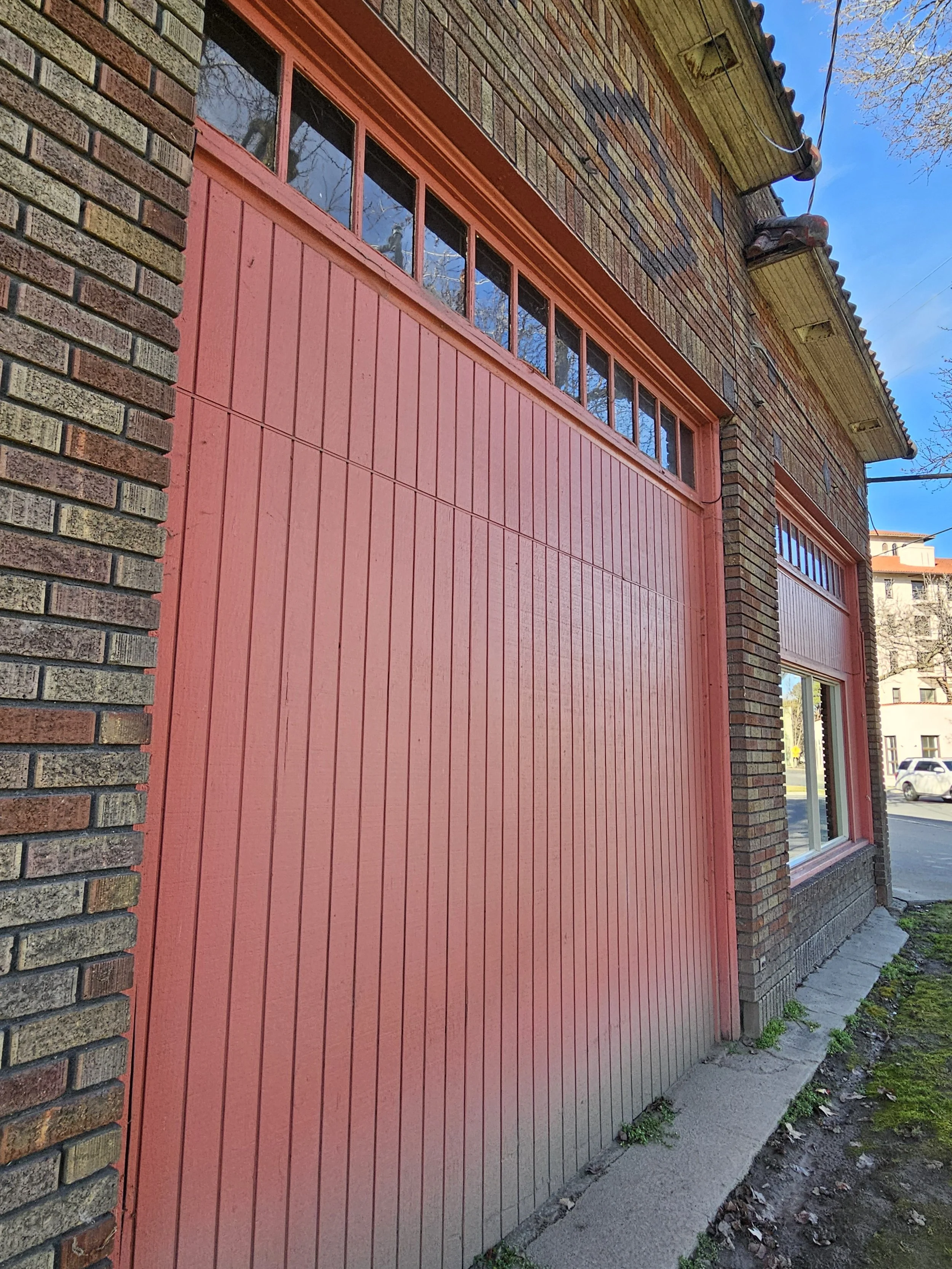 Close-up of a red garage door on a brick house, with a small window at the top and a concrete walkway in front.