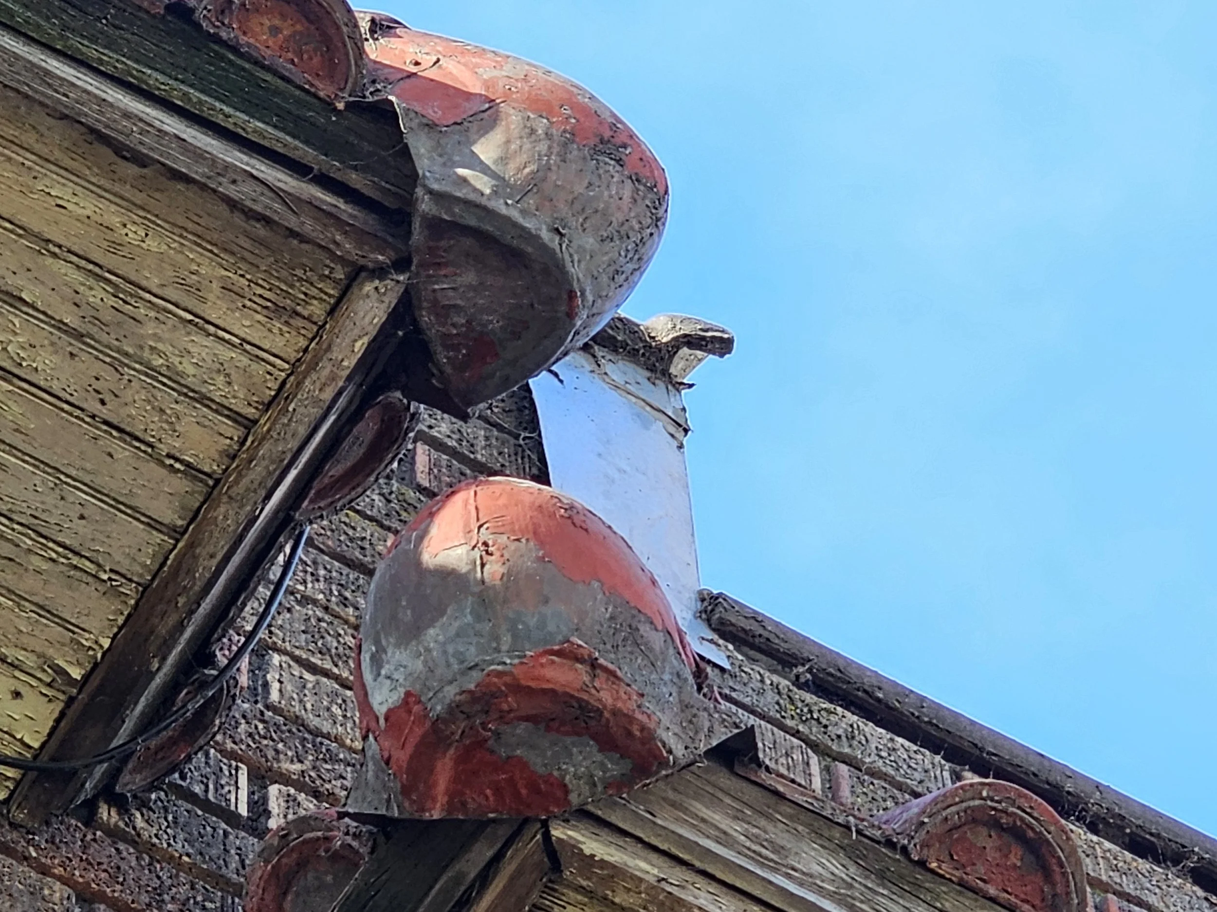 Close-up of the corner of a brick building roof with aged curved red and gray tiles against a blue sky.