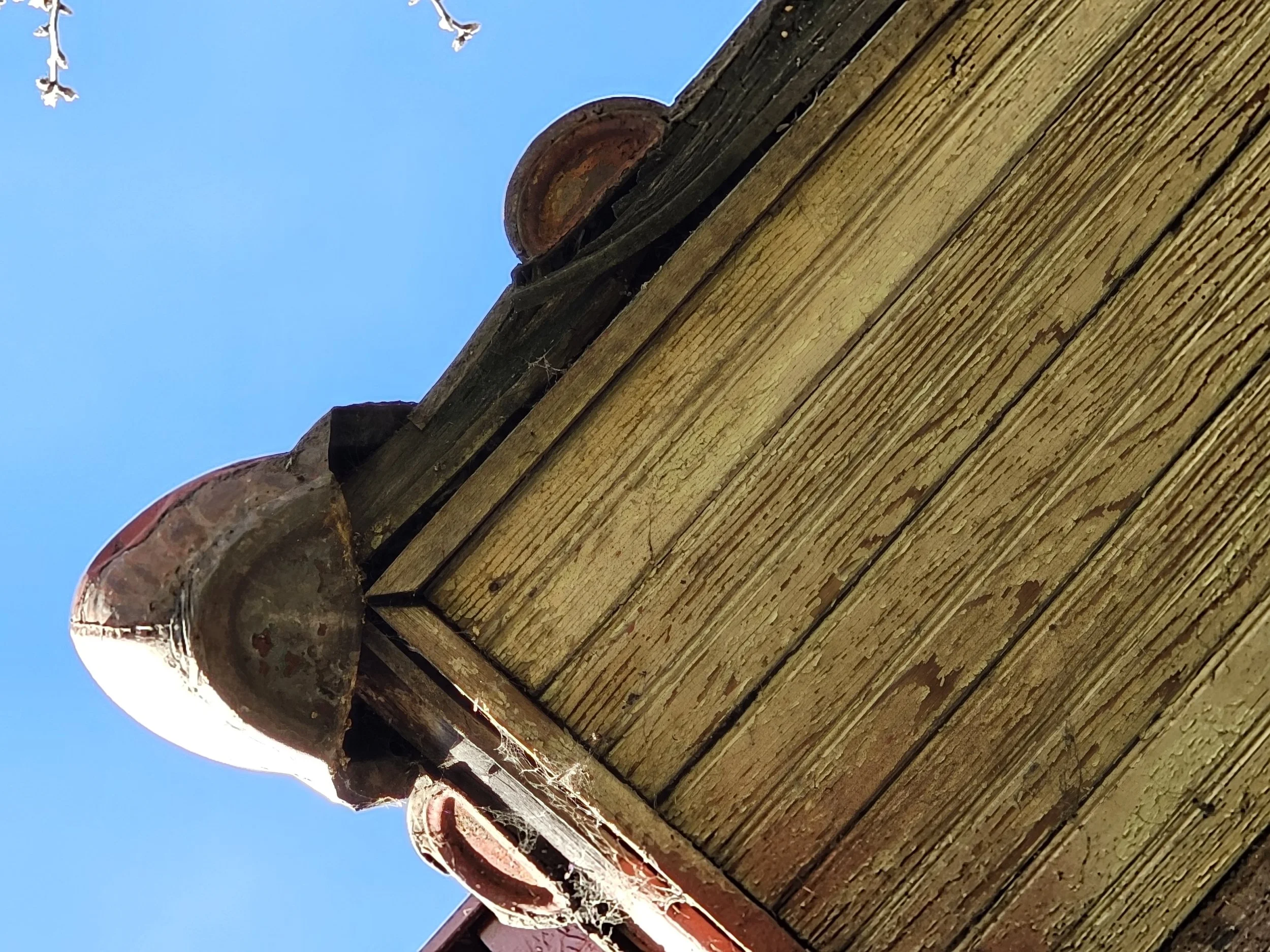 Close-up of a wooden corner of a building with brick tiles and a blue sky in the background.