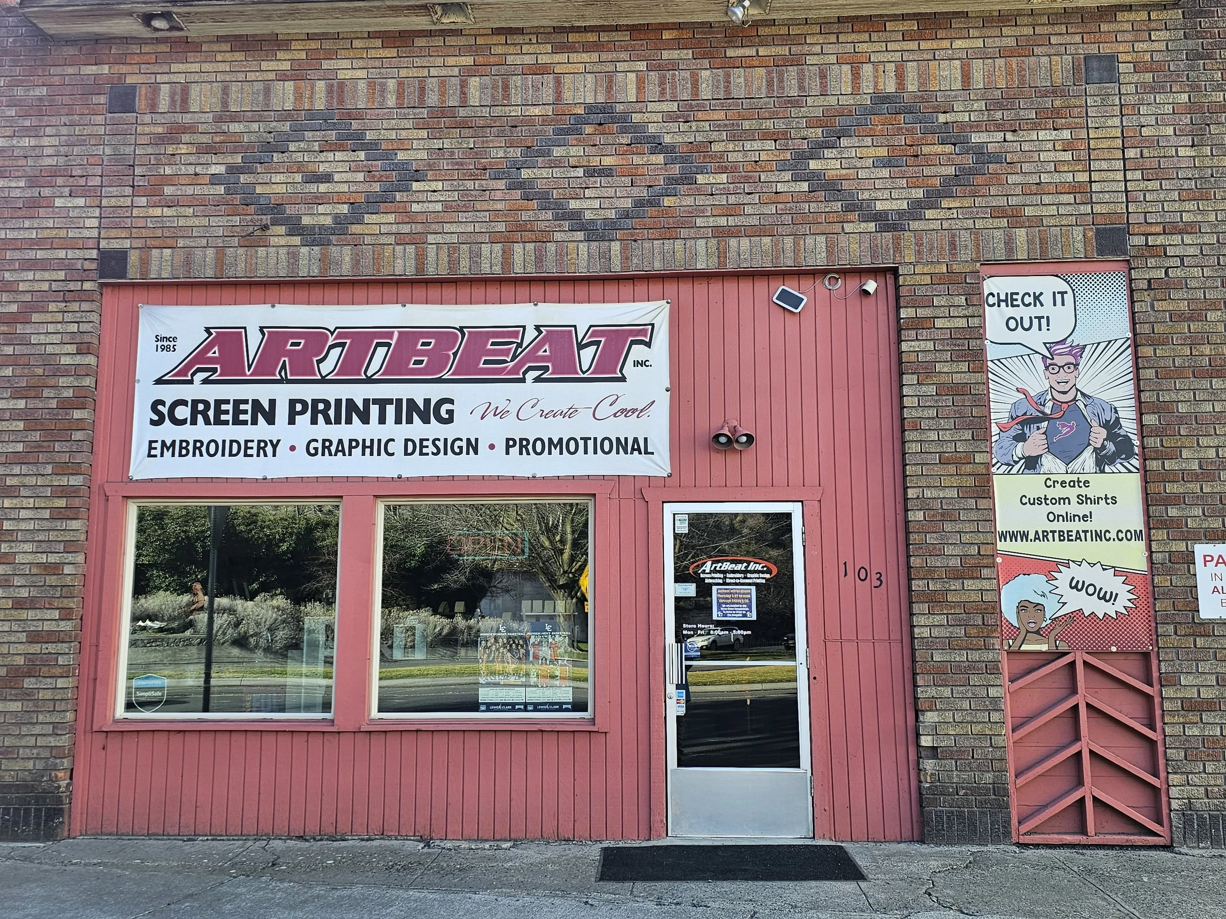  storefront with a large sign that reads 'ARTBEAT INC.' and advertises screen printing, embroidery, graphic design, and promotional services. To the right, a comic-style banner features a superhero character with a speech bubble saying 'CHECK IT OUT!