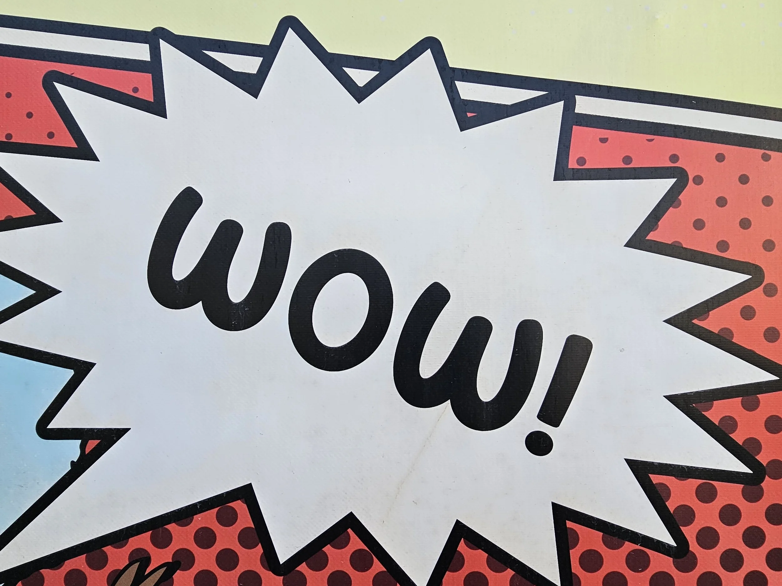 Pop art style sign with the word 'Wow!' in black letters on a white starburst background with red and blue patterned sections.