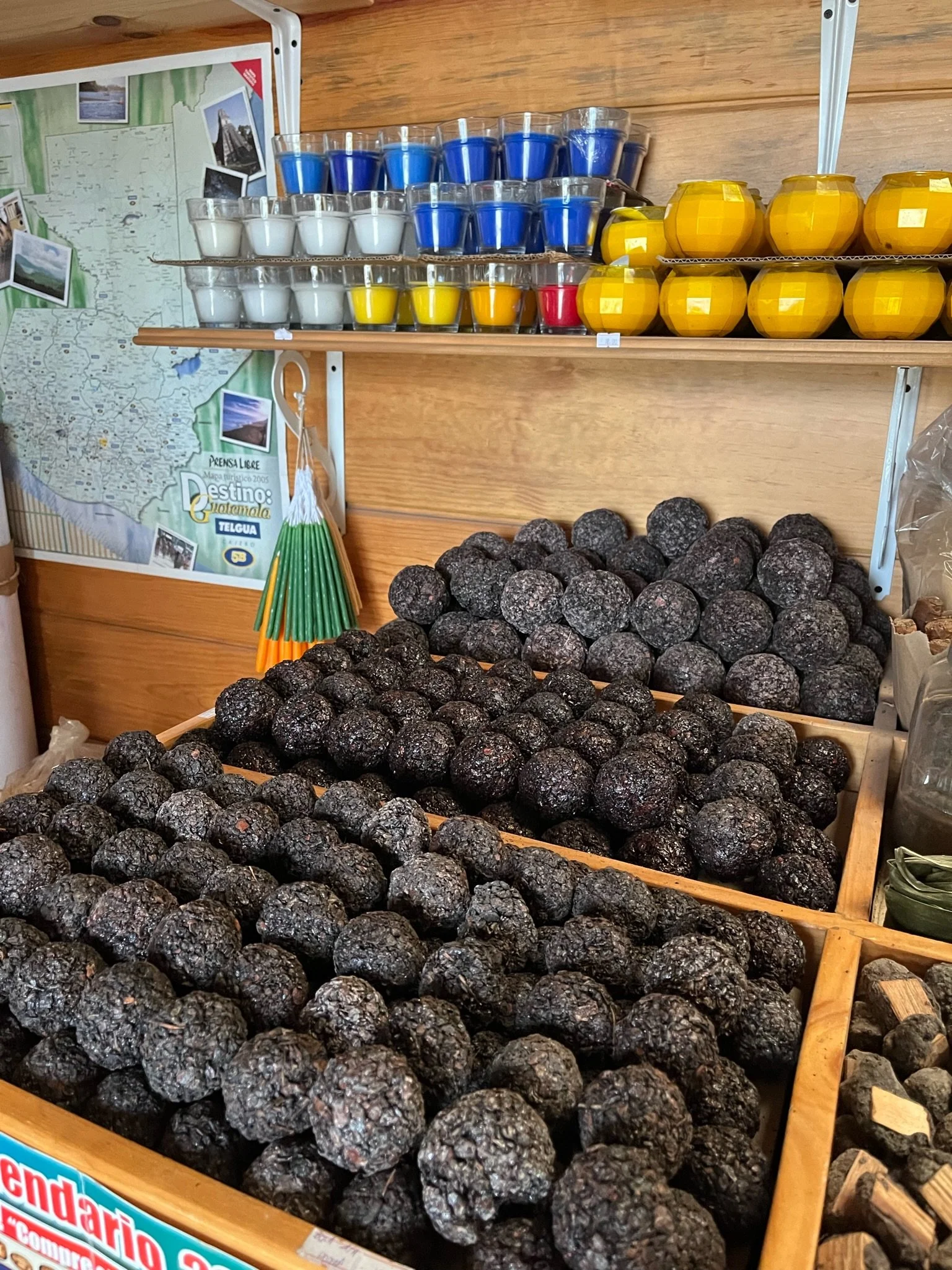 Display of black truffles at a market stall with colorful candles and a map of Guatemala in the background.
