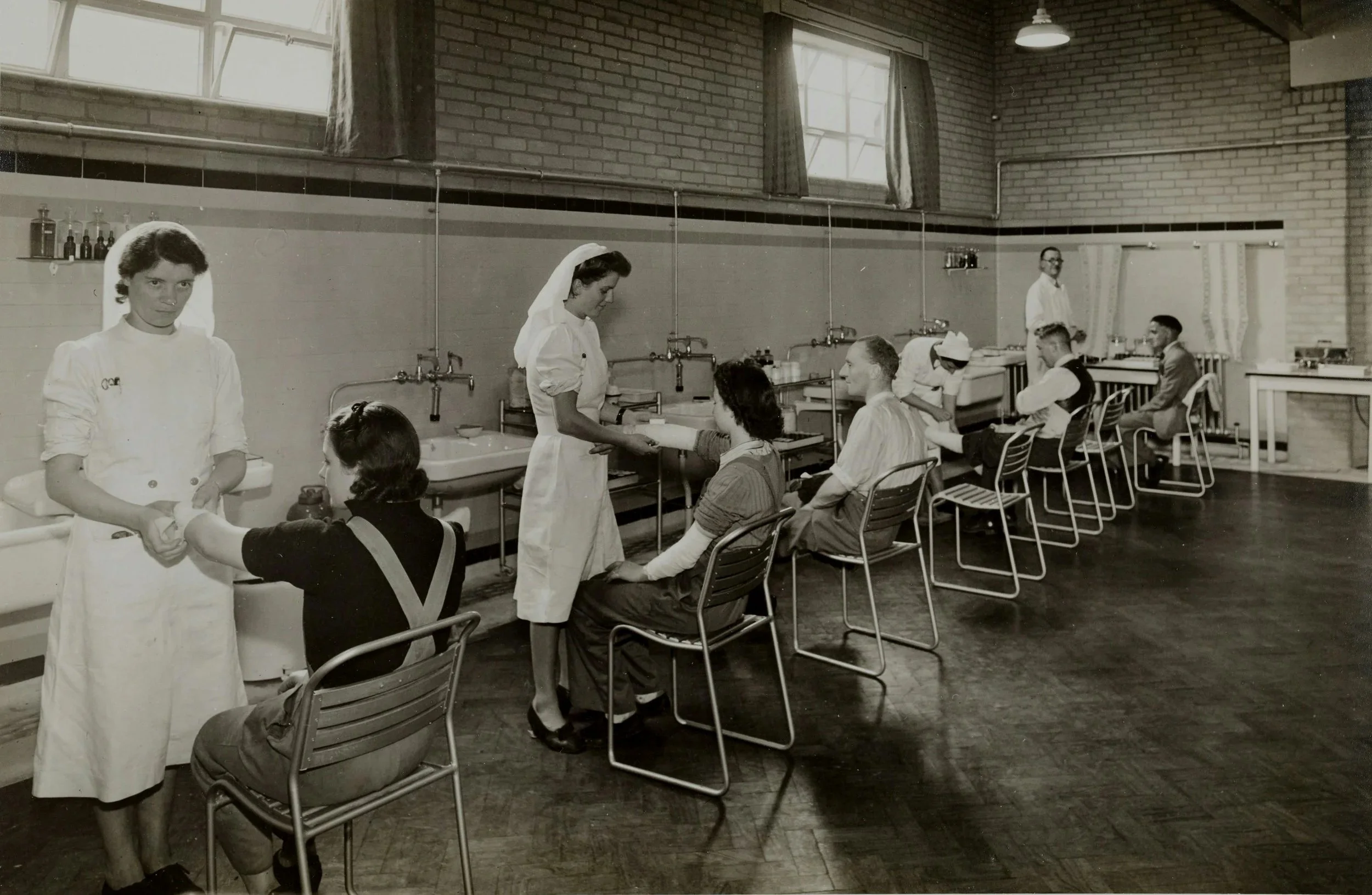 Black-and-white photo of a vintage medical setting, where nurses are taking blood from seated patients in a line.