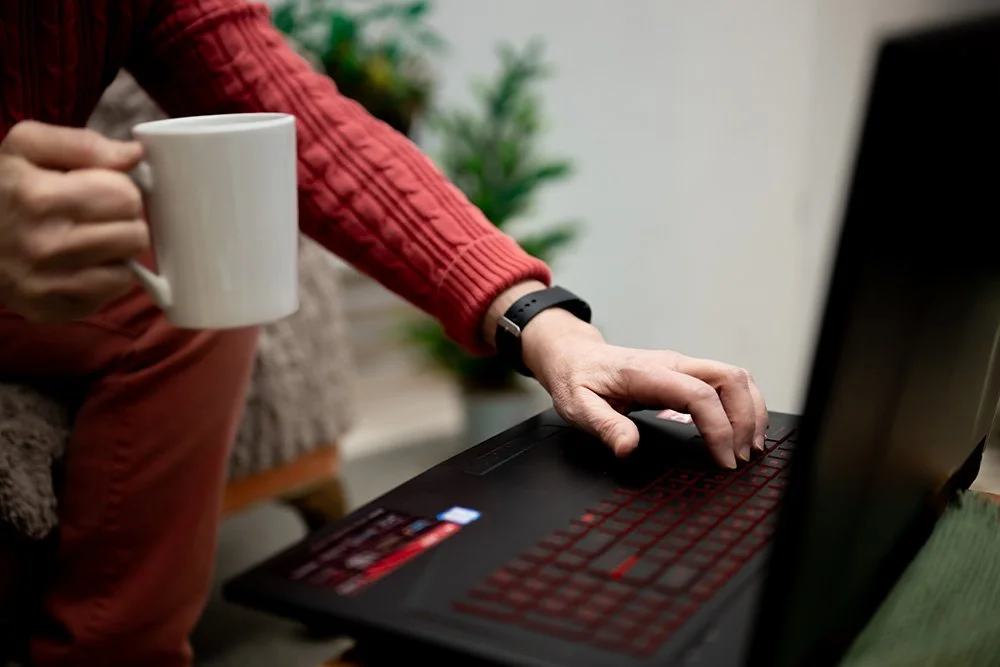 Rural Nurse Writer Dana Plank's hands, 1 typing on a computer and the other holding a mug