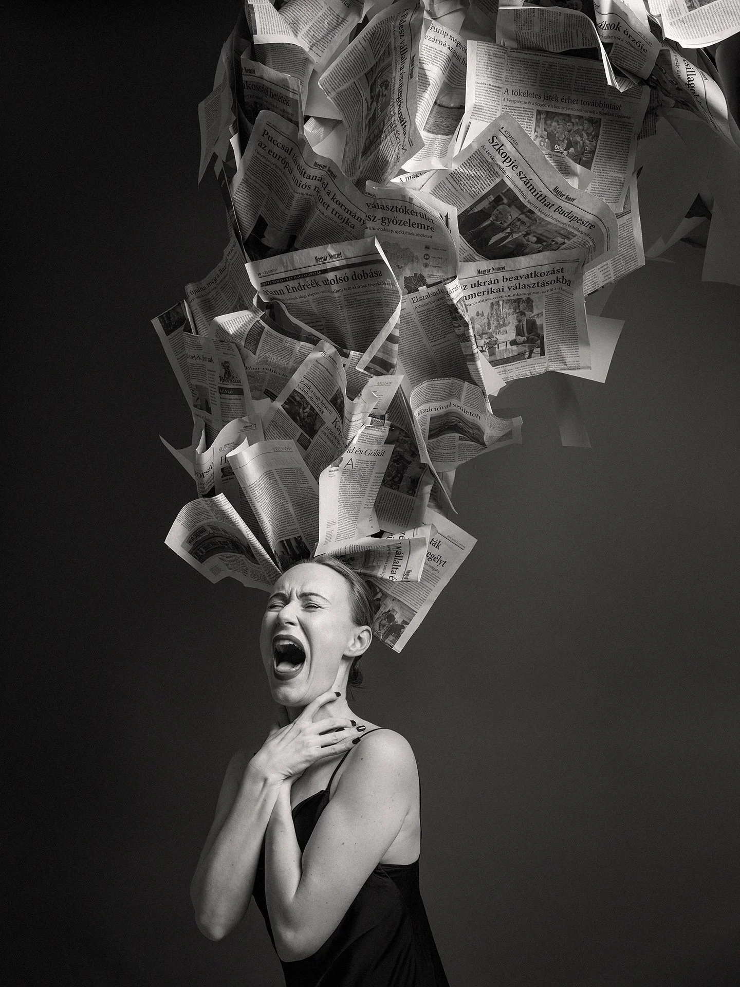 Black and white photo of a woman with her mouth open and eyes closed, with her hand on her neck and the other arm crossed over her chest. Newspapers are flying above her head, creating a dramatic scene.