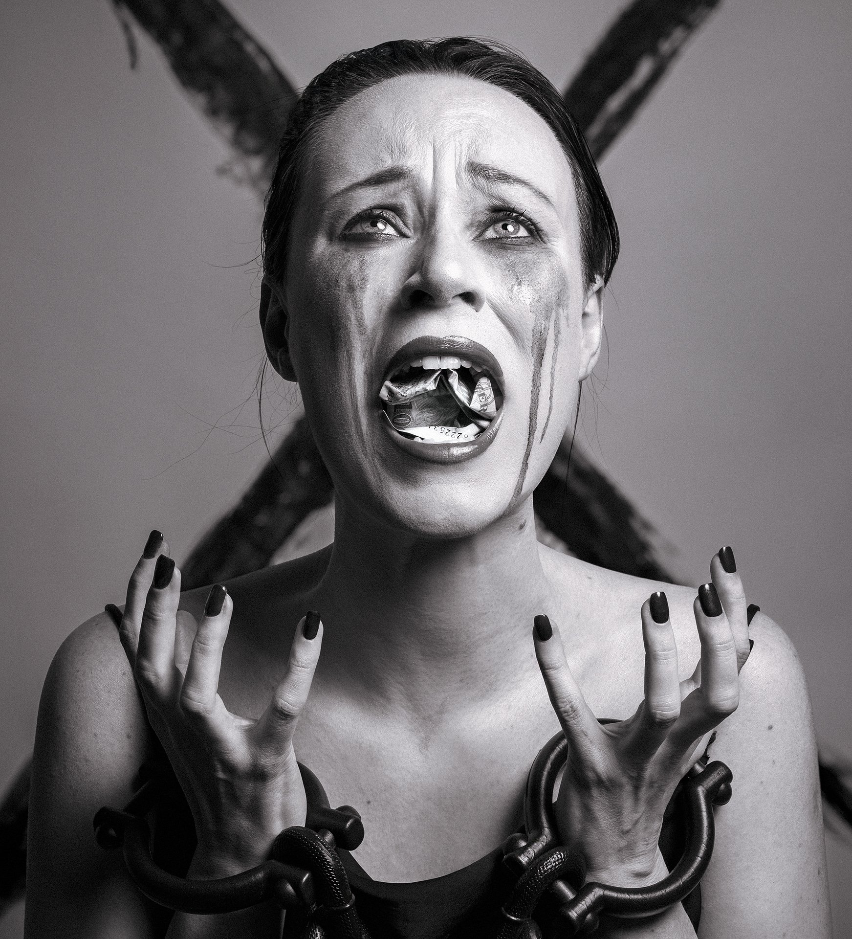 Black and white photo of a woman with dark hair, appearing distressed with tears running down her face, mouth open, and fingers raised. She is surrounded by large, dark, flexible hoses or tubes.