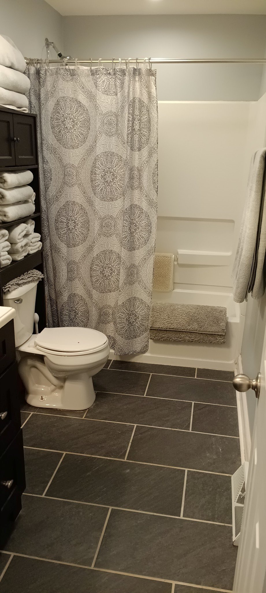 Modern bathroom with white toilet, patterned shower curtain, and shelves with folded towels.
