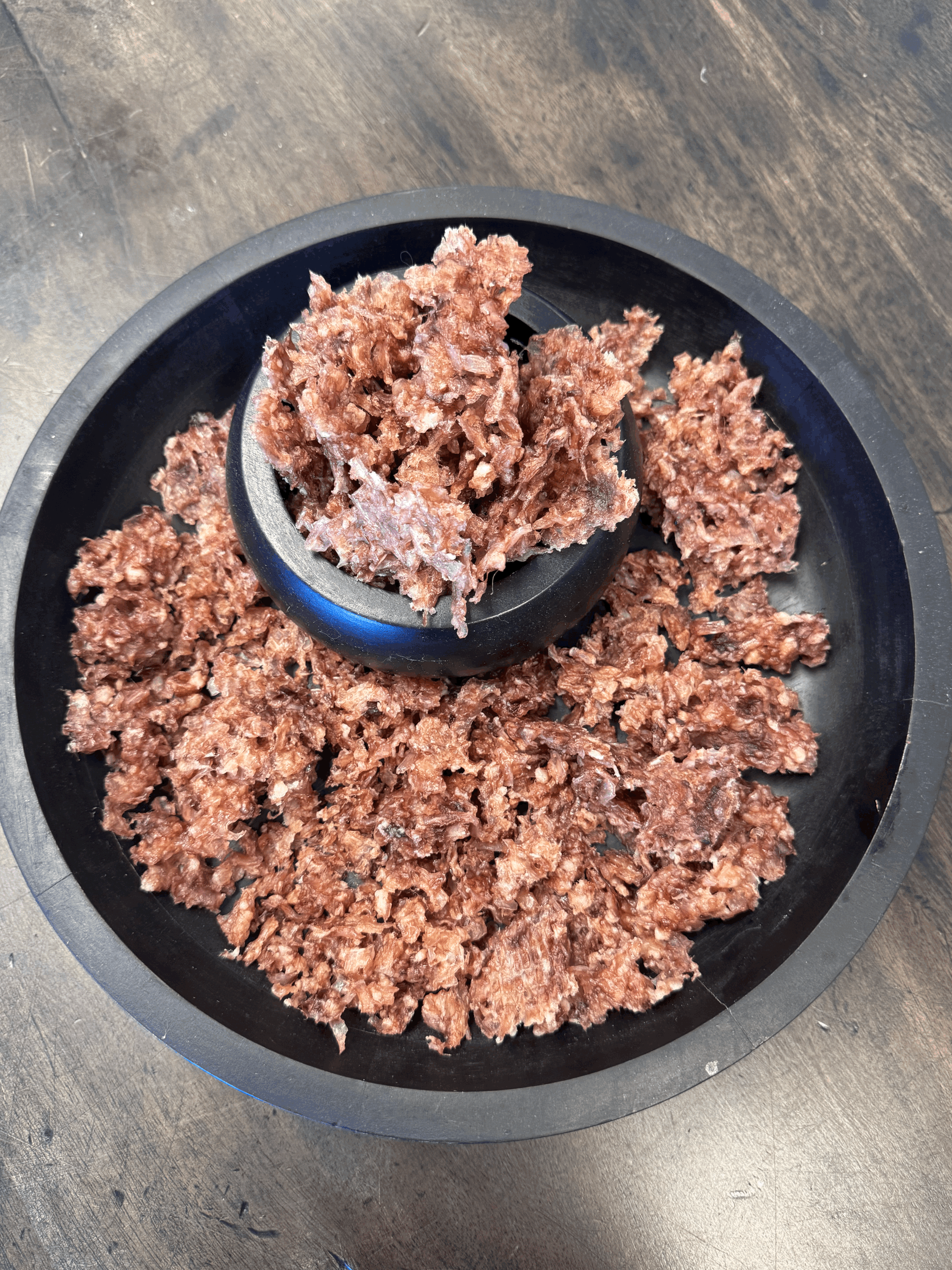 Close-up of Air-Dried Lamb Trachea Crumble in a black bowl, with textured pieces spread across a black platter.