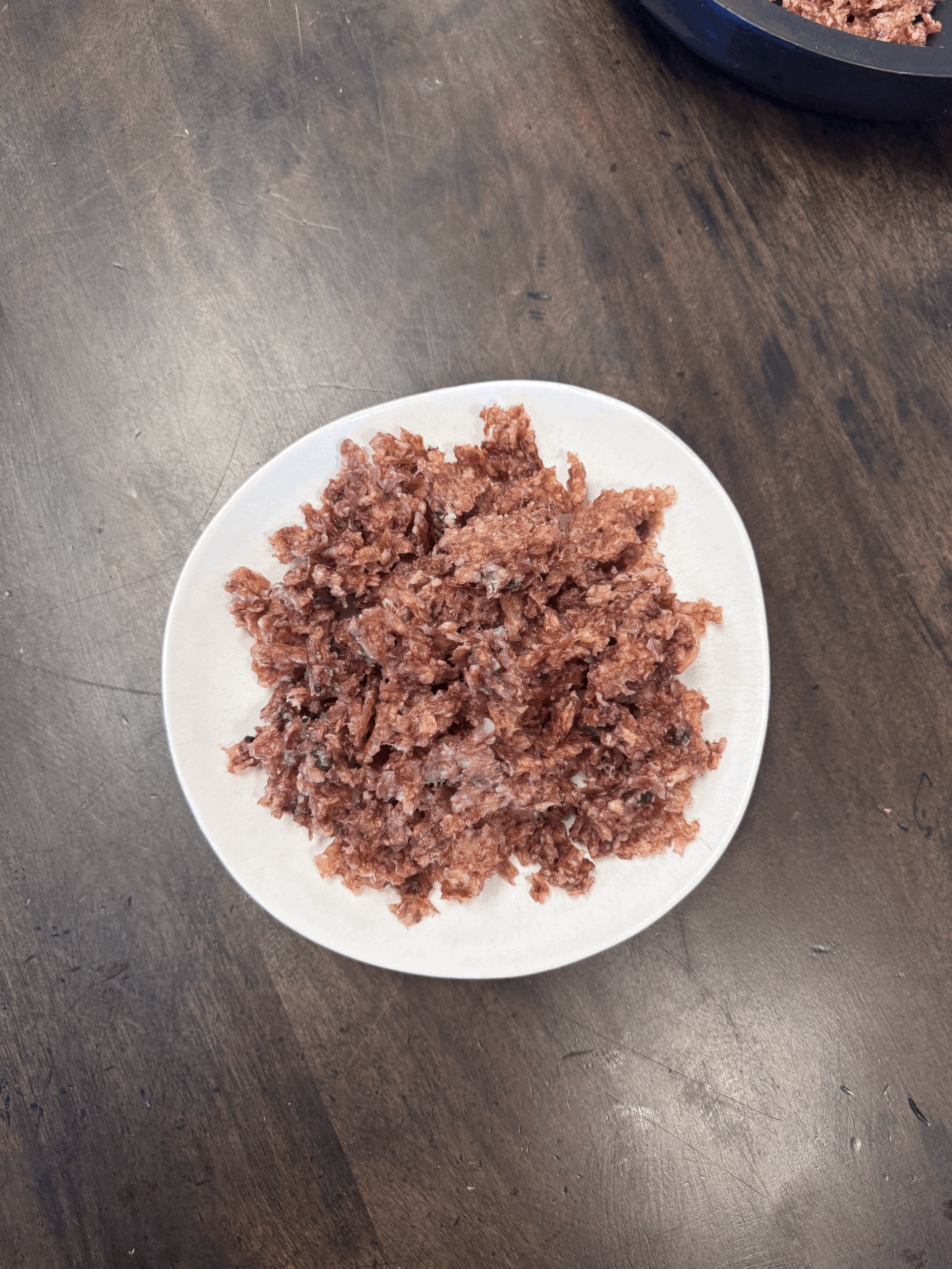 Air-Dried Lamb Trachea Crumble piled on a white plate on a dark wooden table.