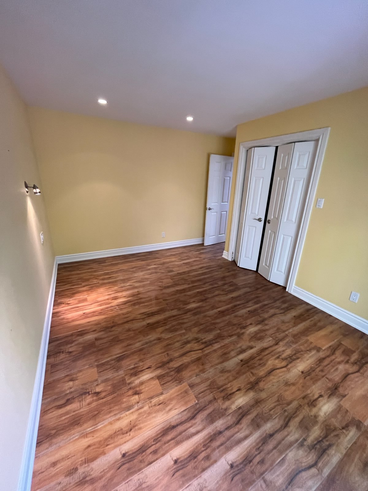 Empty room with wood flooring, yellow walls, white trim, and doors, with ceiling lights.