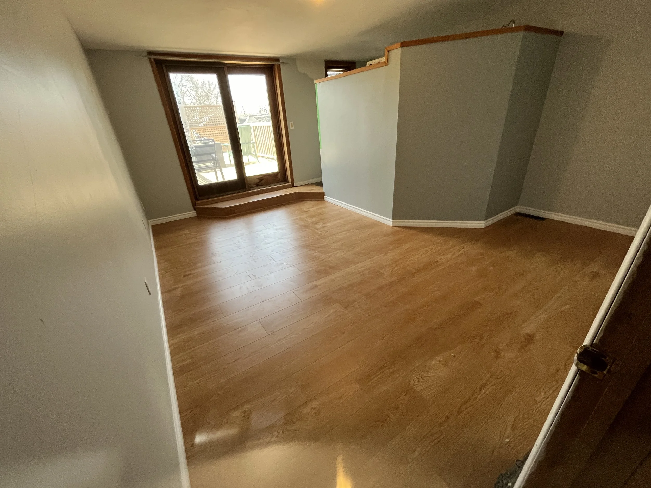 A room with wooden flooring, a sliding glass door leading to an outdoor patio, and a half wall with a wooden top.