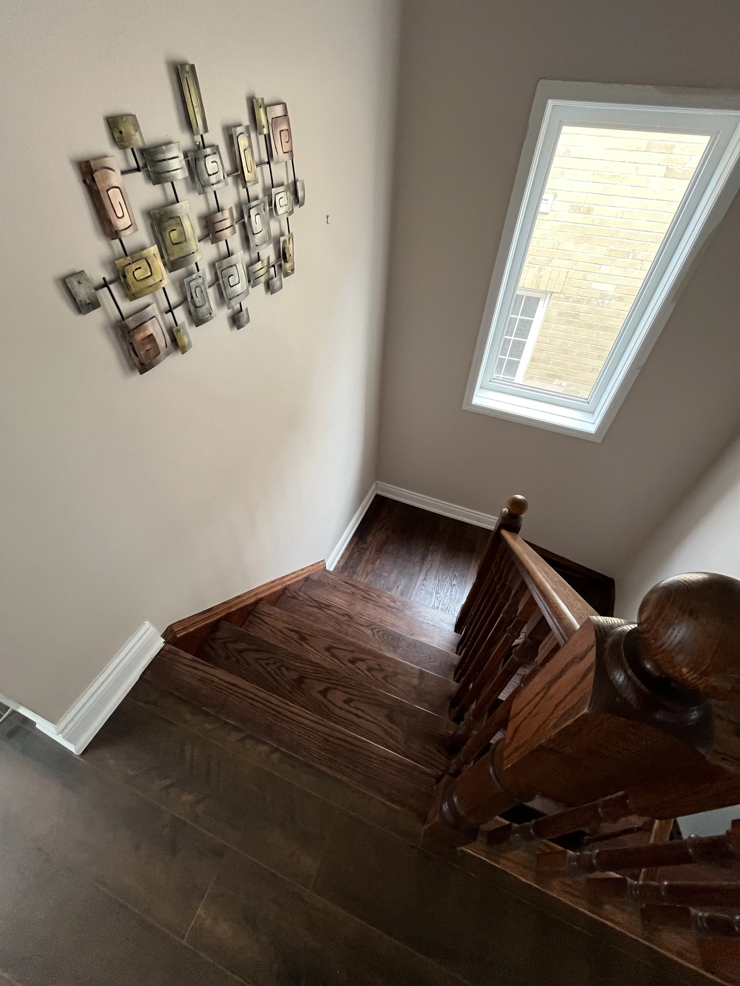 A staircase with wooden steps and a wooden handrail, beige wall, decorative wall art, and a skylight window with a view of a brick building outside.