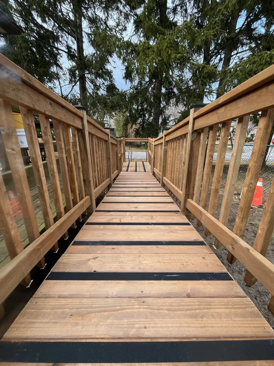 Wooden walkway with railings on both sides, surrounded by trees and construction site in the background.