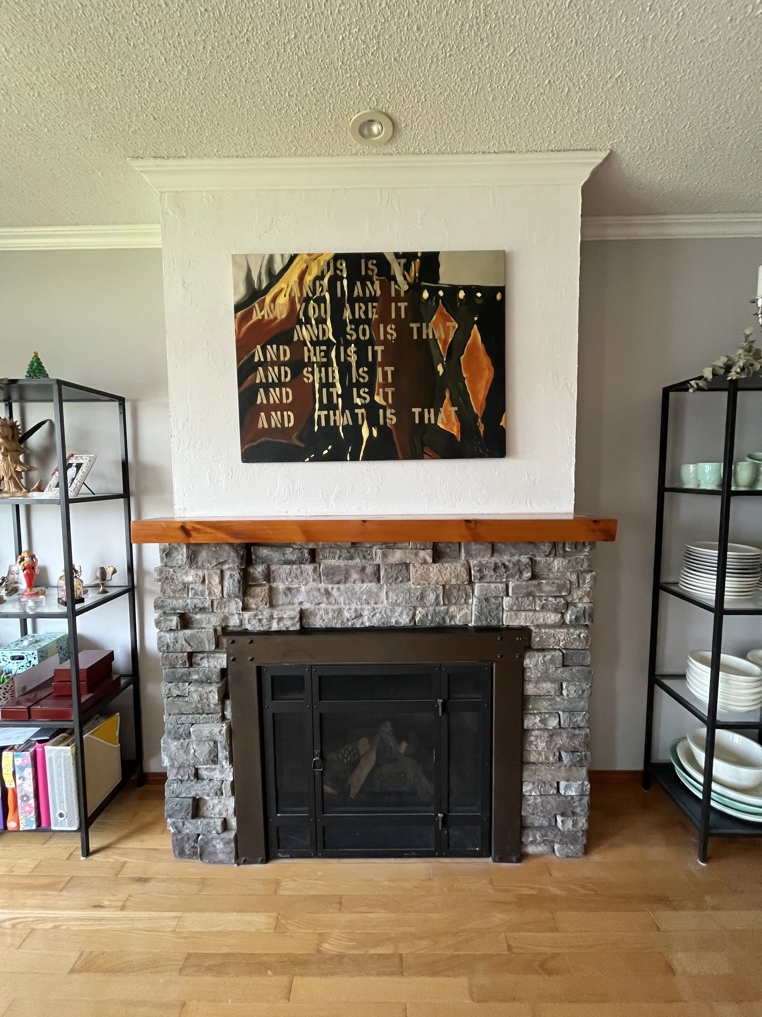 Living room with stone fireplace, artwork above it, and black metal shelves on sides holding plates and decorations.