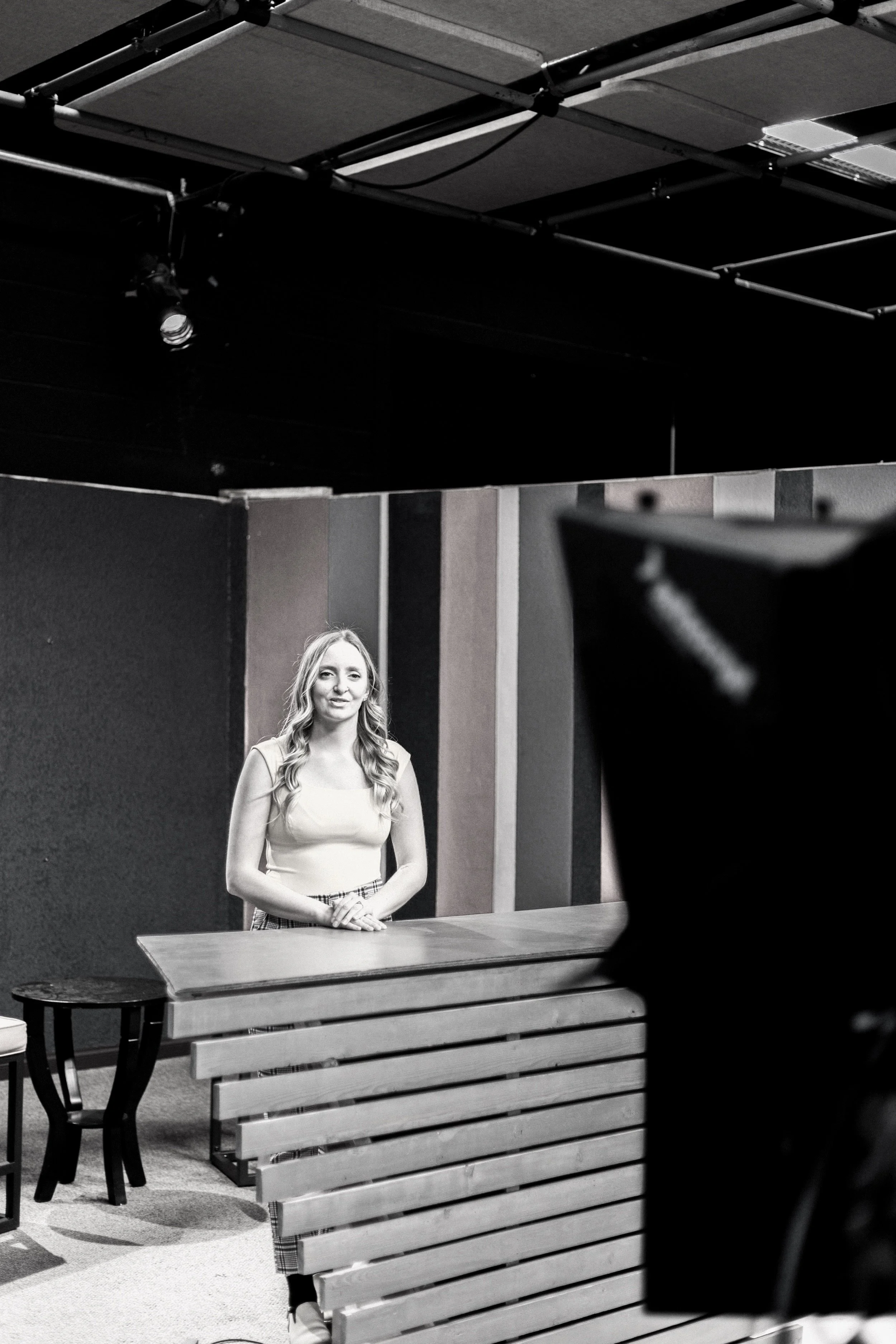 Person standing behind a table in a studio setup, with lighting equipment and a backdrop.
