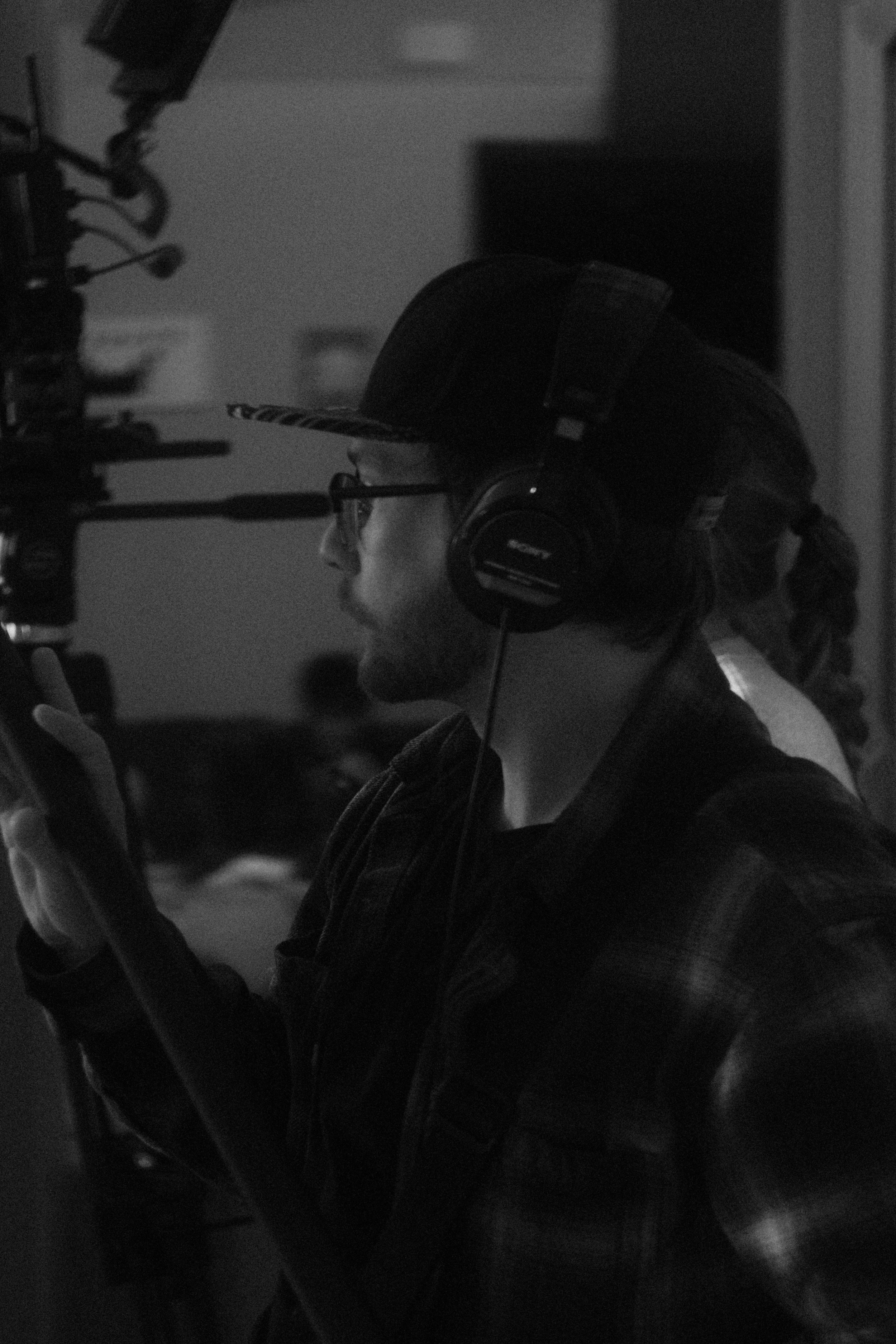 Person wearing headphones operating a camera in a dimly lit setting.