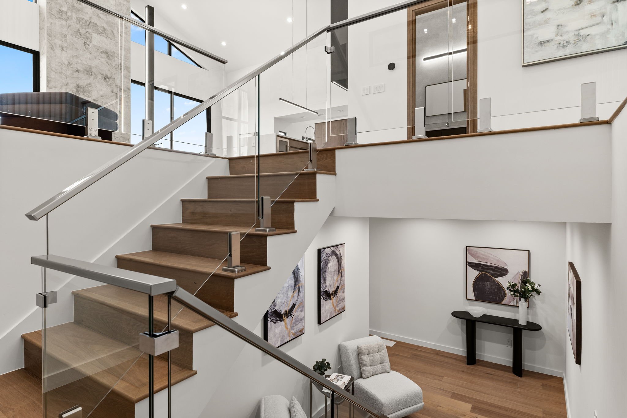 Modern interior with a wooden staircase, glass railing, abstract art, and minimalist furniture.