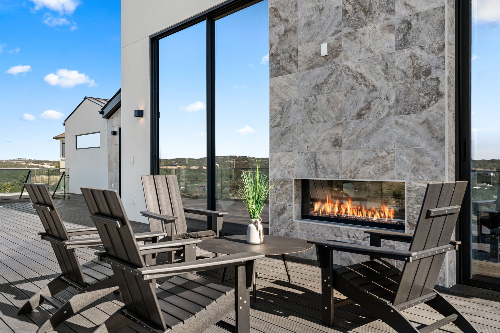 Outdoor patio with modern fireplace, black wooden chairs, circular table, and mountain view.
