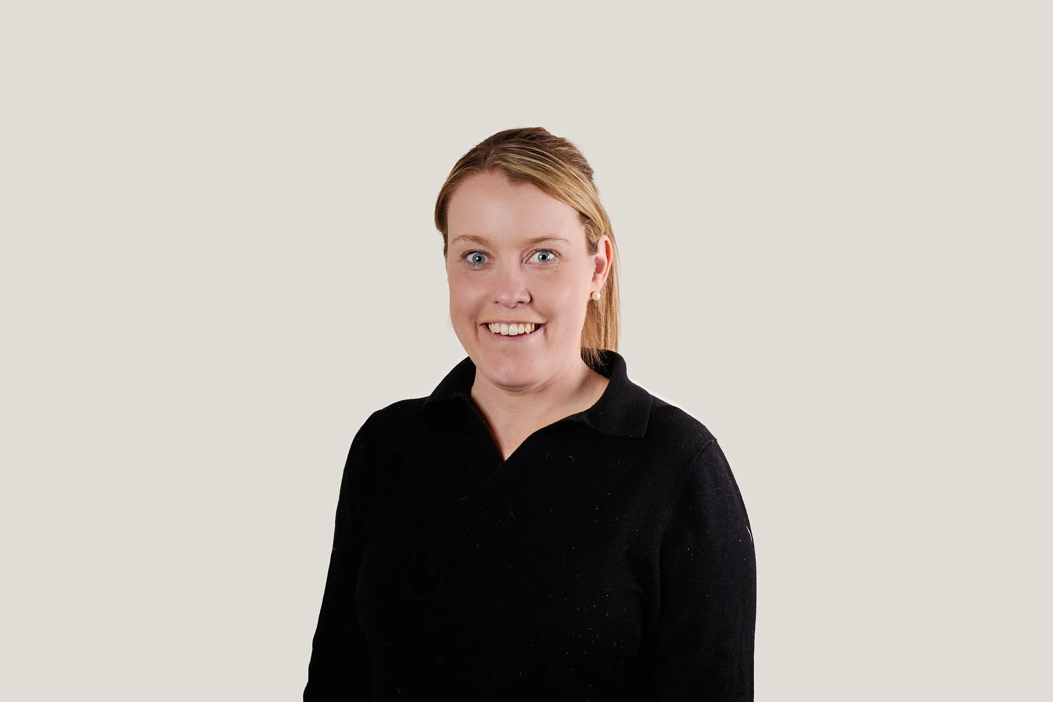 A woman with red hair, wearing a black collared shirt, smiling against a plain light background.