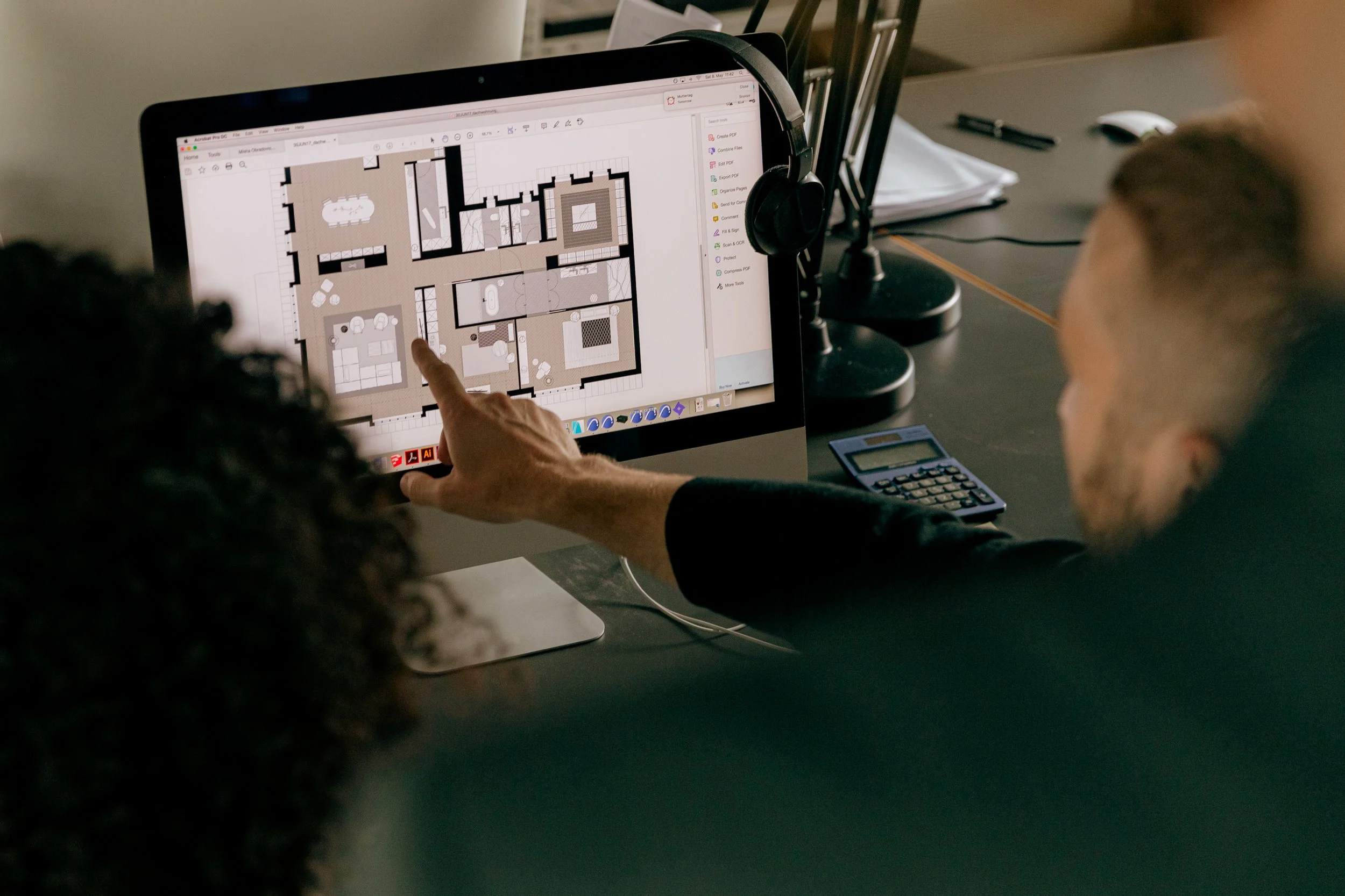 Two people looking at a computer screen displaying a detailed floor plan or architectural layout of a building.