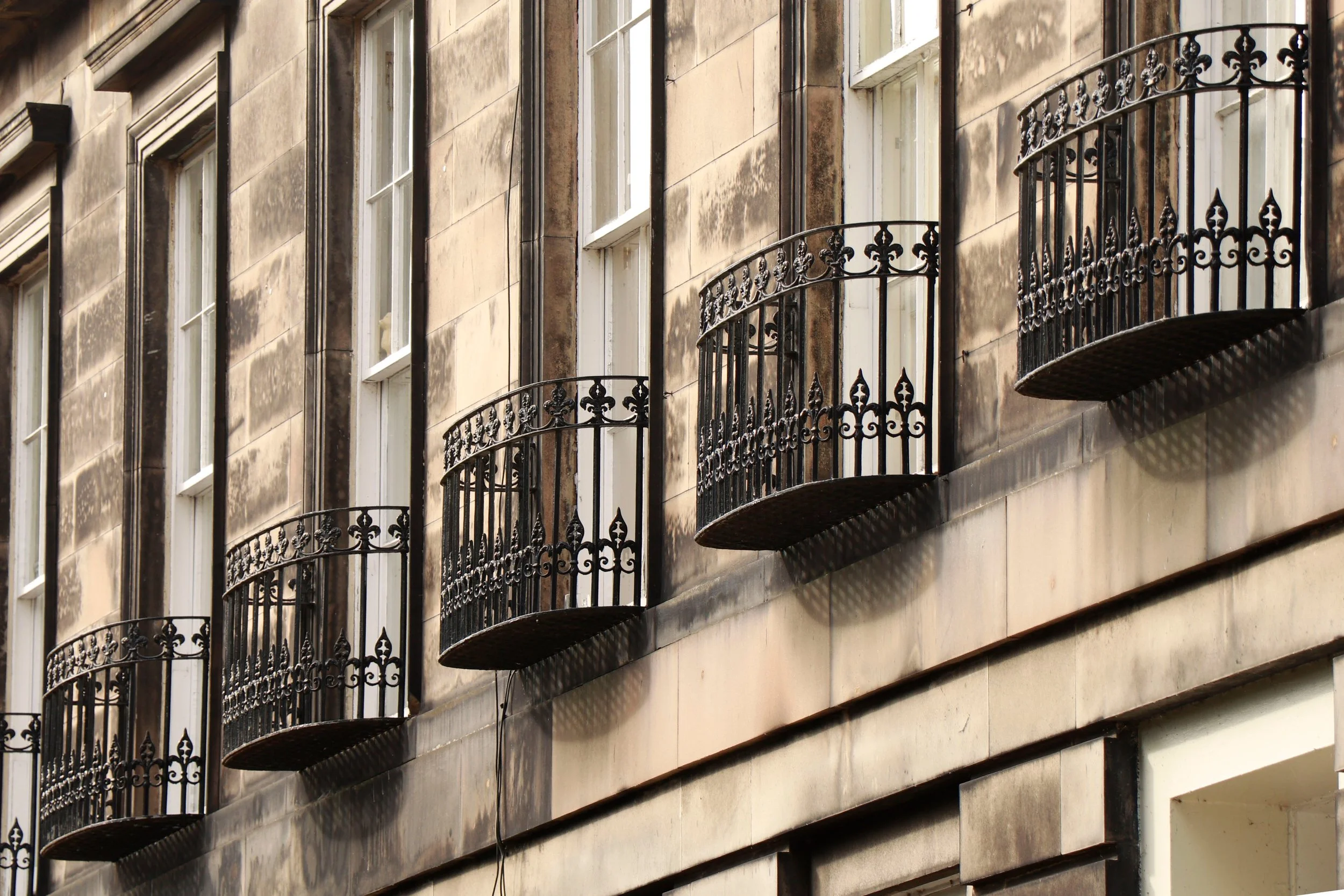 Multiple factory new, off-white color building with small, decorative black wrought iron balconies on the facade.