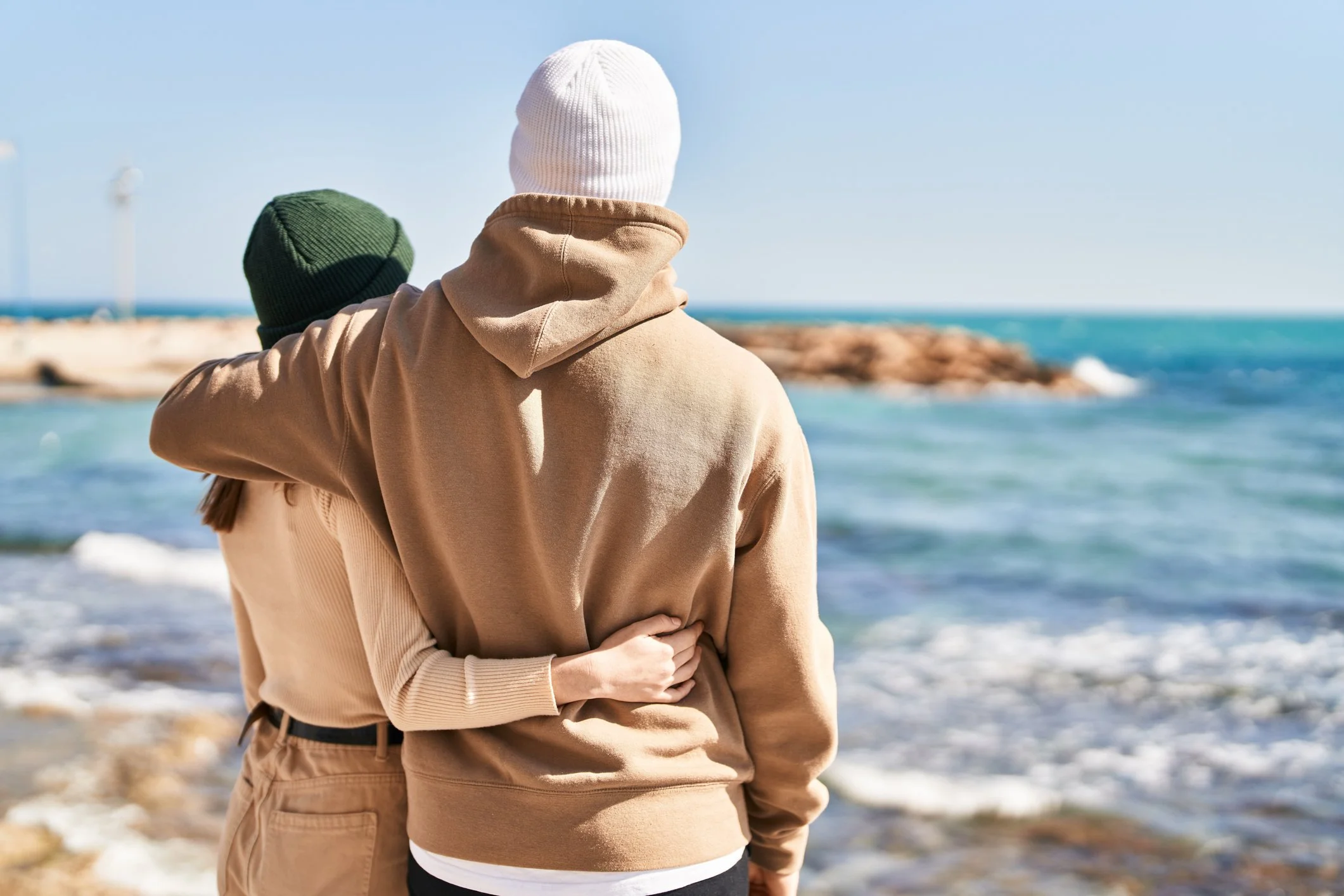 A couple looking at the ocean and embracing on the beach, reflecting after therapy session. Finding calm.