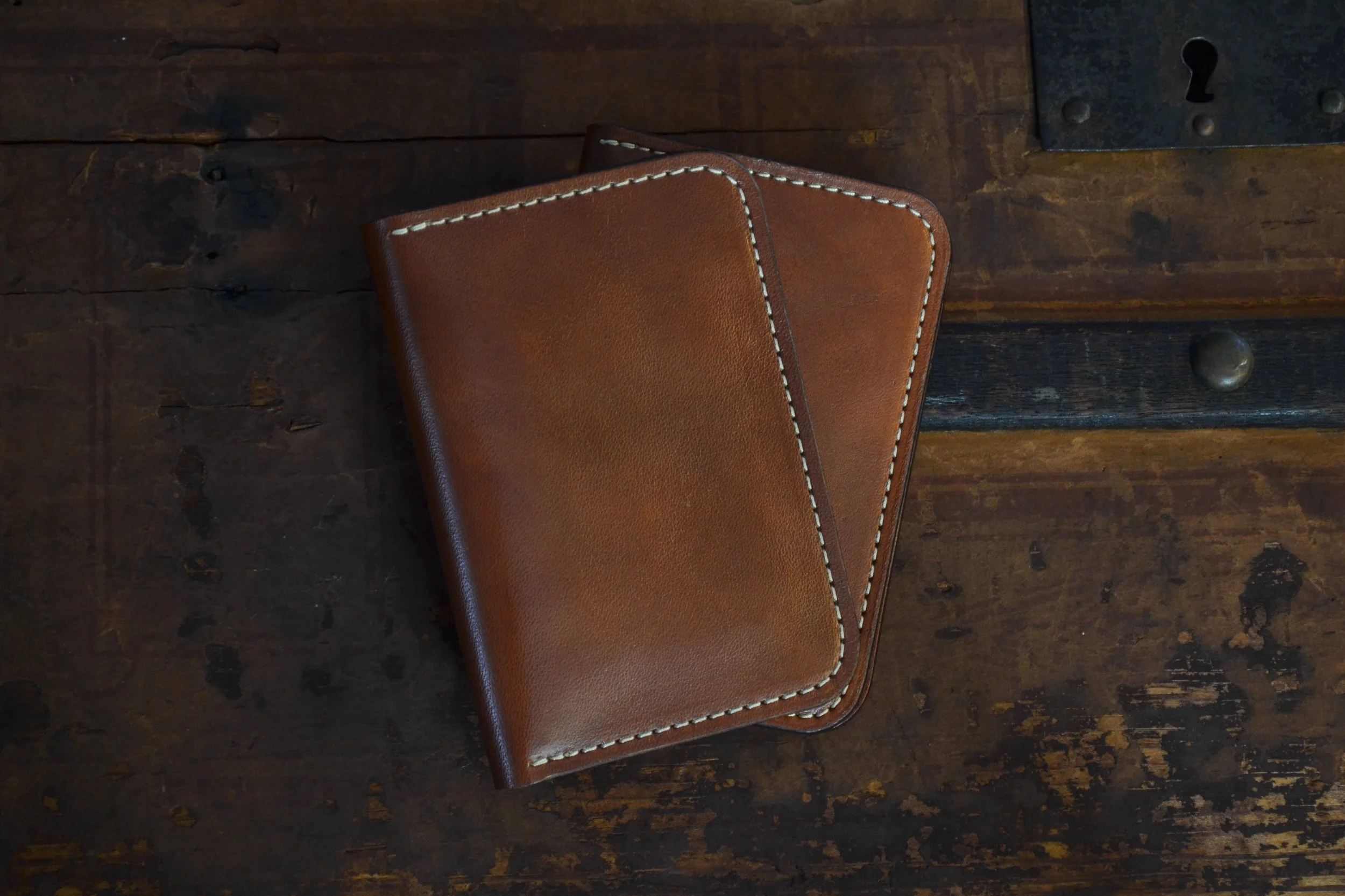 A brown leather wallet with white stitching resting on a dark wooden surface.