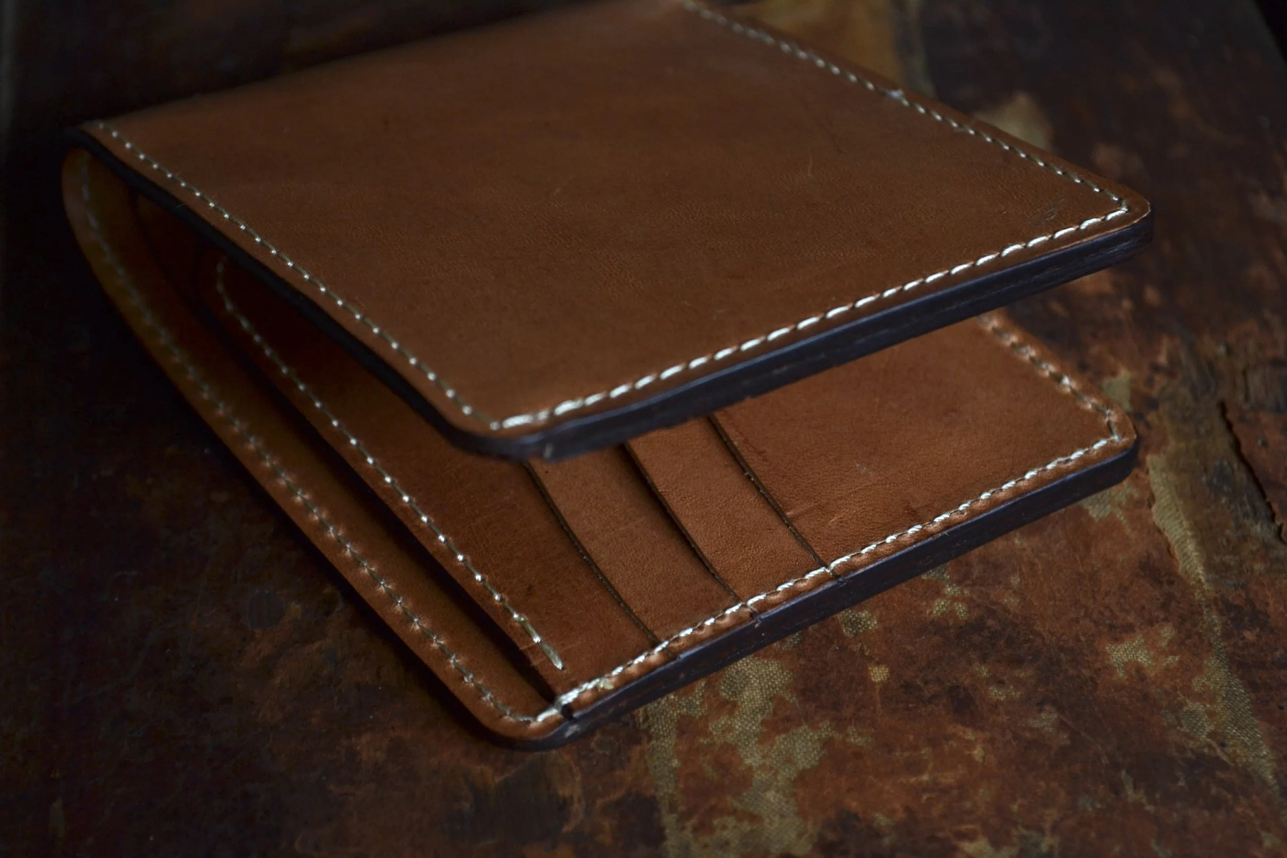 A brown leather wallet with white stitching, open to reveal card slots, placed on a dark textured surface.