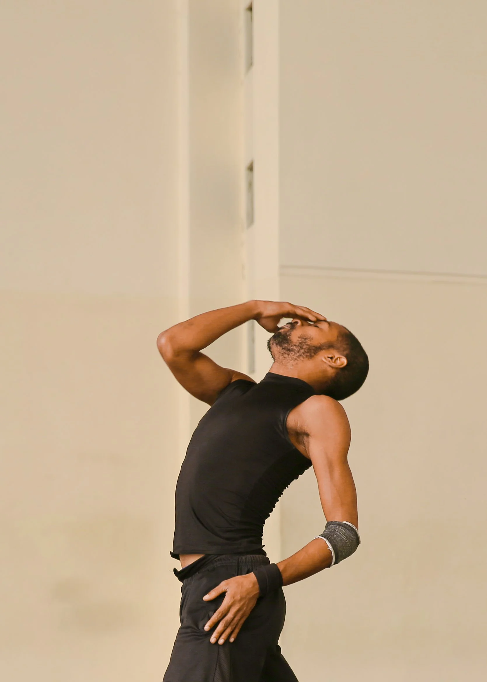 A man in athletic clothing stretches or warms up against a plain beige wall.