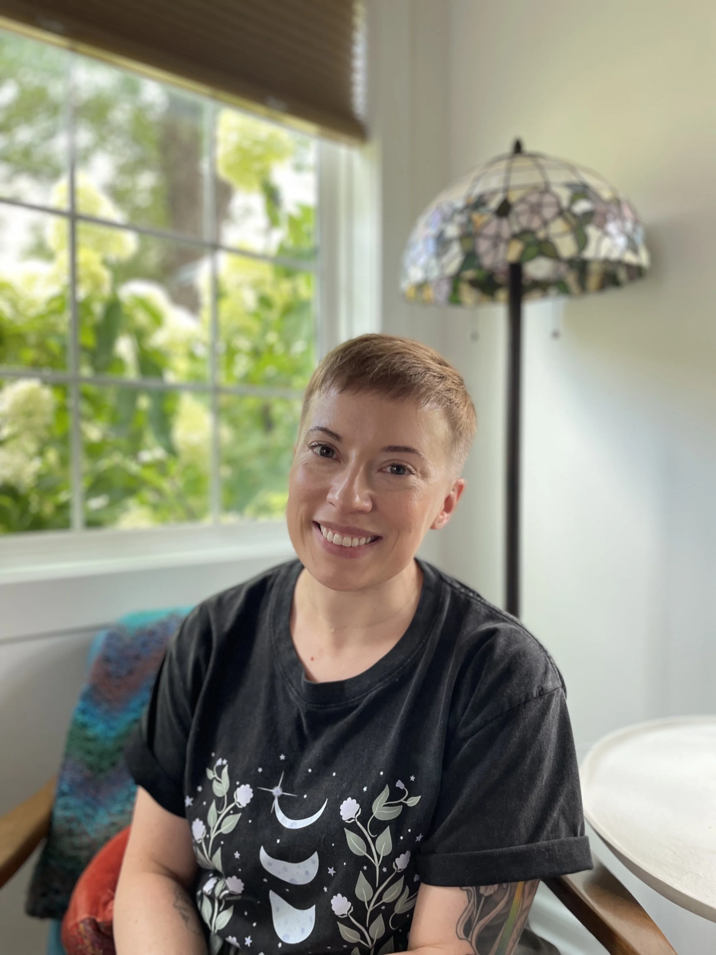 Kelley Iris seated in front of a sunny window, smiling.
