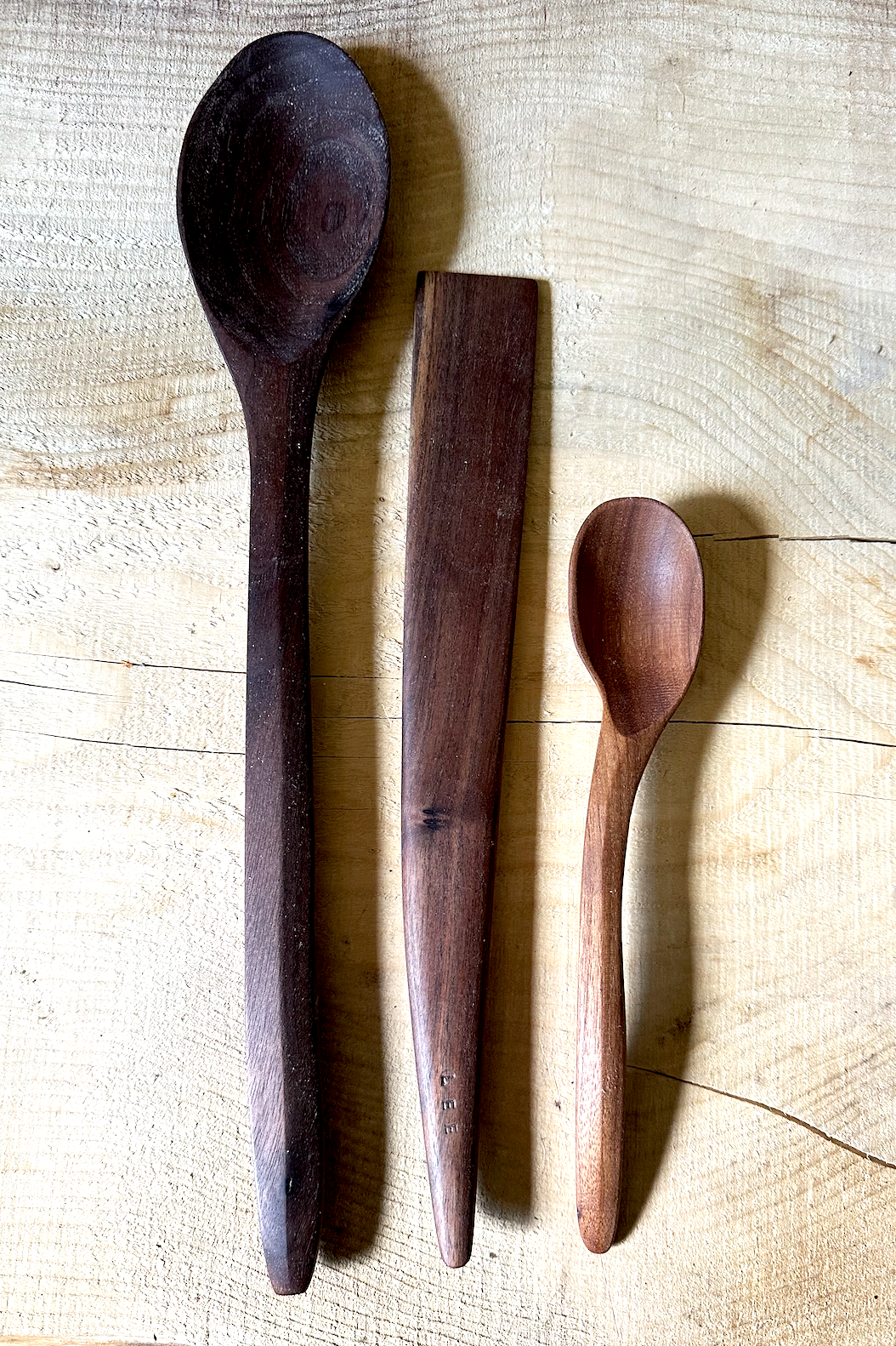 Three wooden spoons of different sizes and shapes on a light wooden surface.