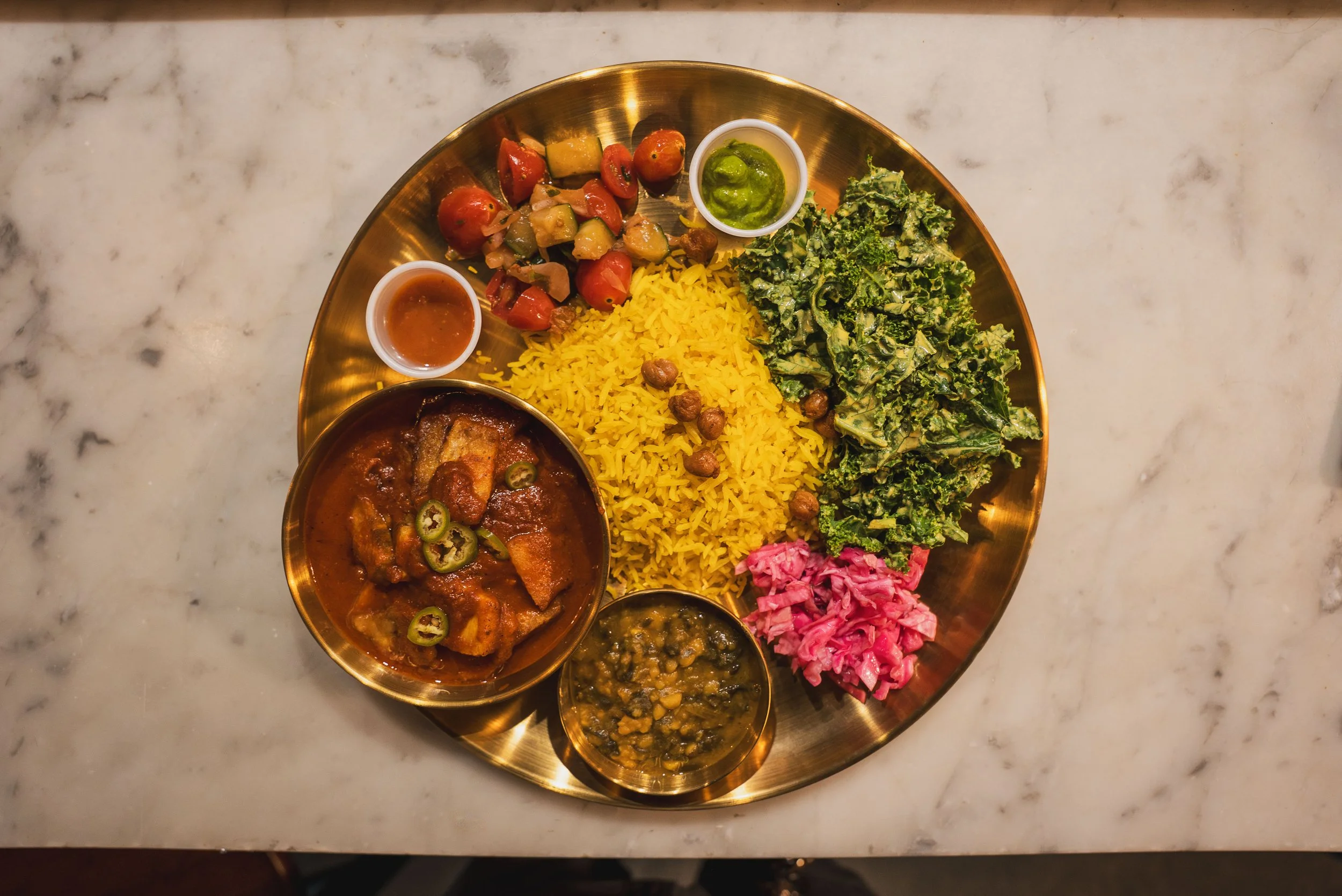 A gold platter with yellow rice, various vegetable dishes, and sauces on a marble surface.