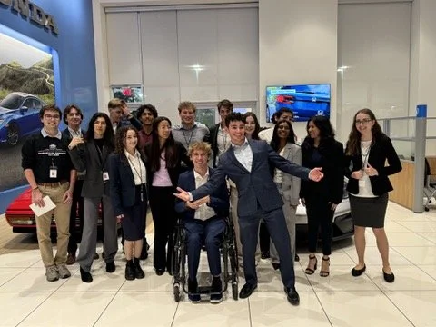 Group of young adults at an electronics store, with one person in a wheelchair, posing for a photo.