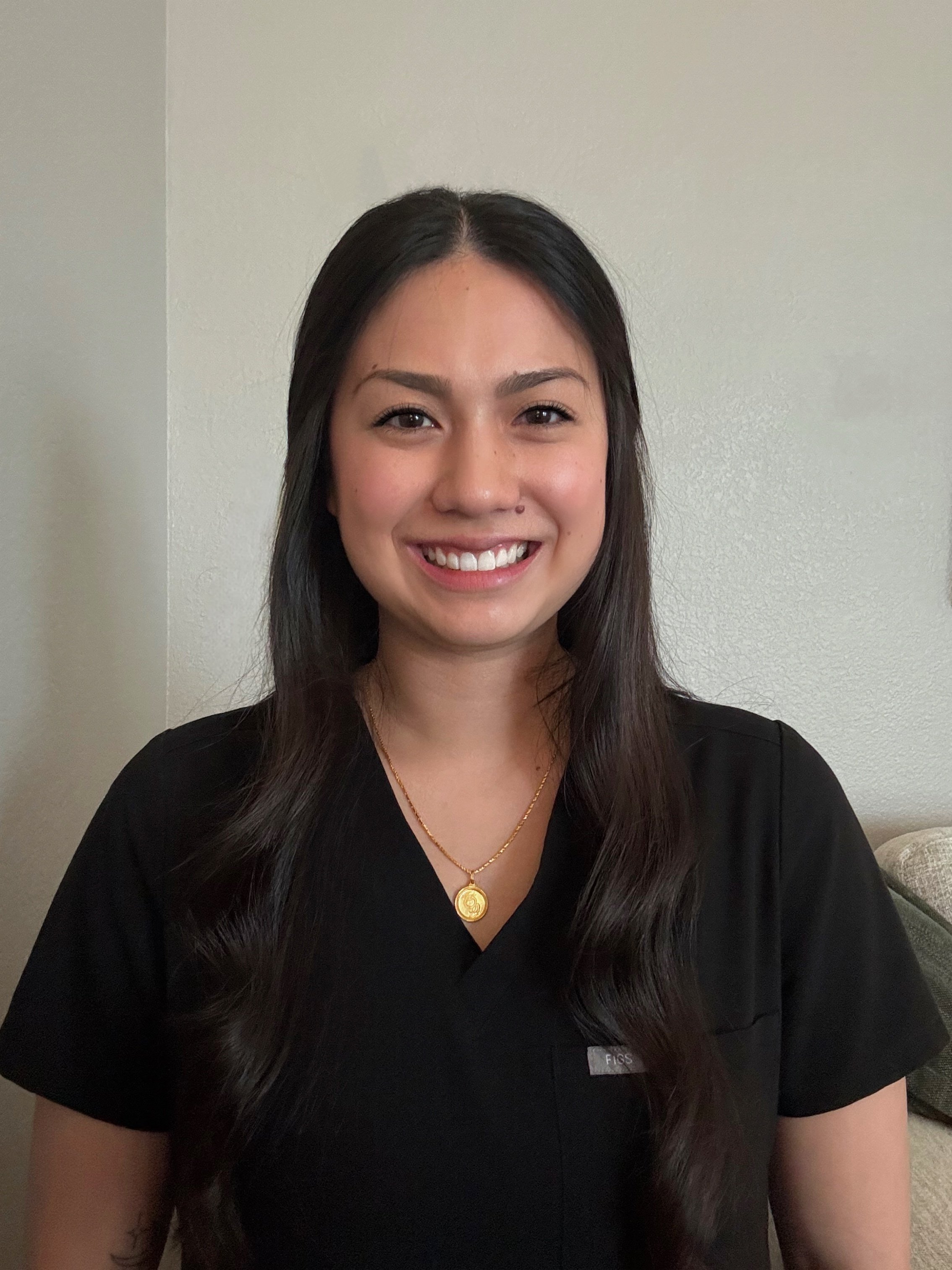 Woman with long black hair wearing black scrubs and gold necklace