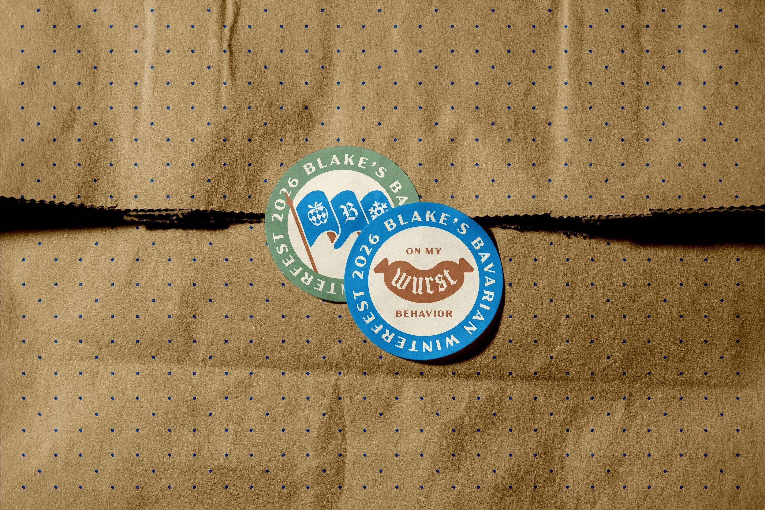 Two circular stickers on a brown paper bag. The stickers say "2026 Blake's Barbados" and "2026 Blake's Barbados on my worst behavior," with one featuring a beach scene and the other a dog silhouette.