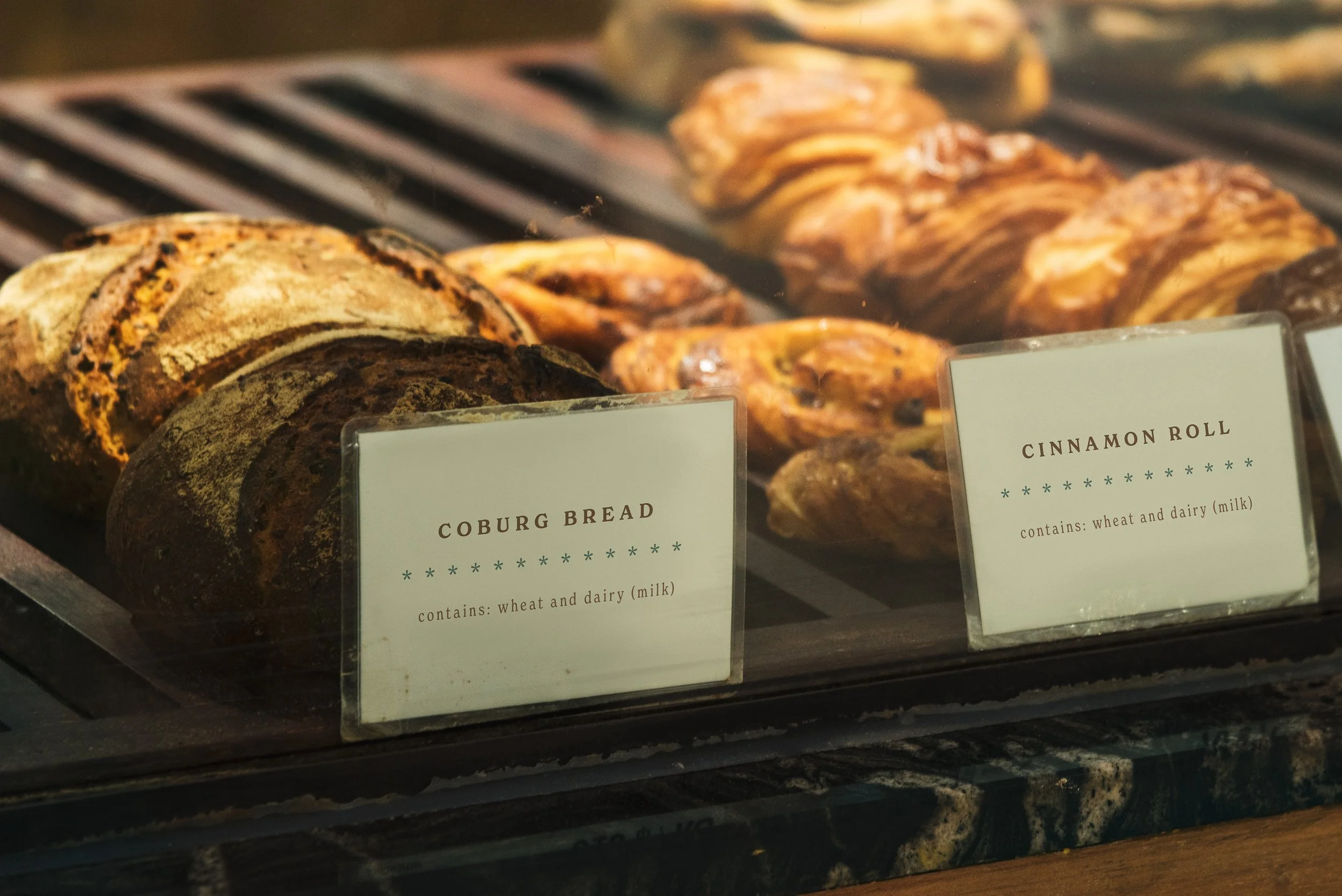Bakery display with Coburg bread and cinnamon rolls labeled with ingredients.