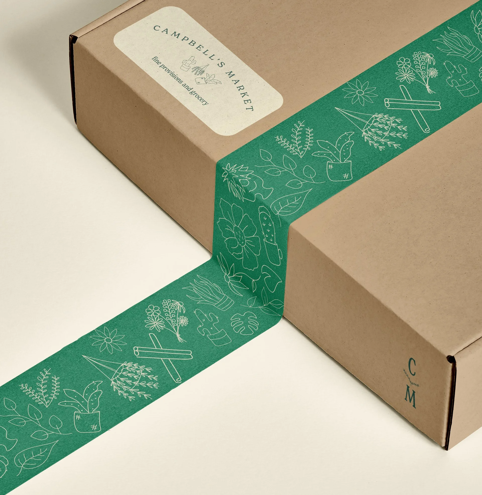 Brown cardboard box with green decorative tape featuring botanical illustrations. The box has a label reading "Campbell's Market: Fine Provisions and Grocery."