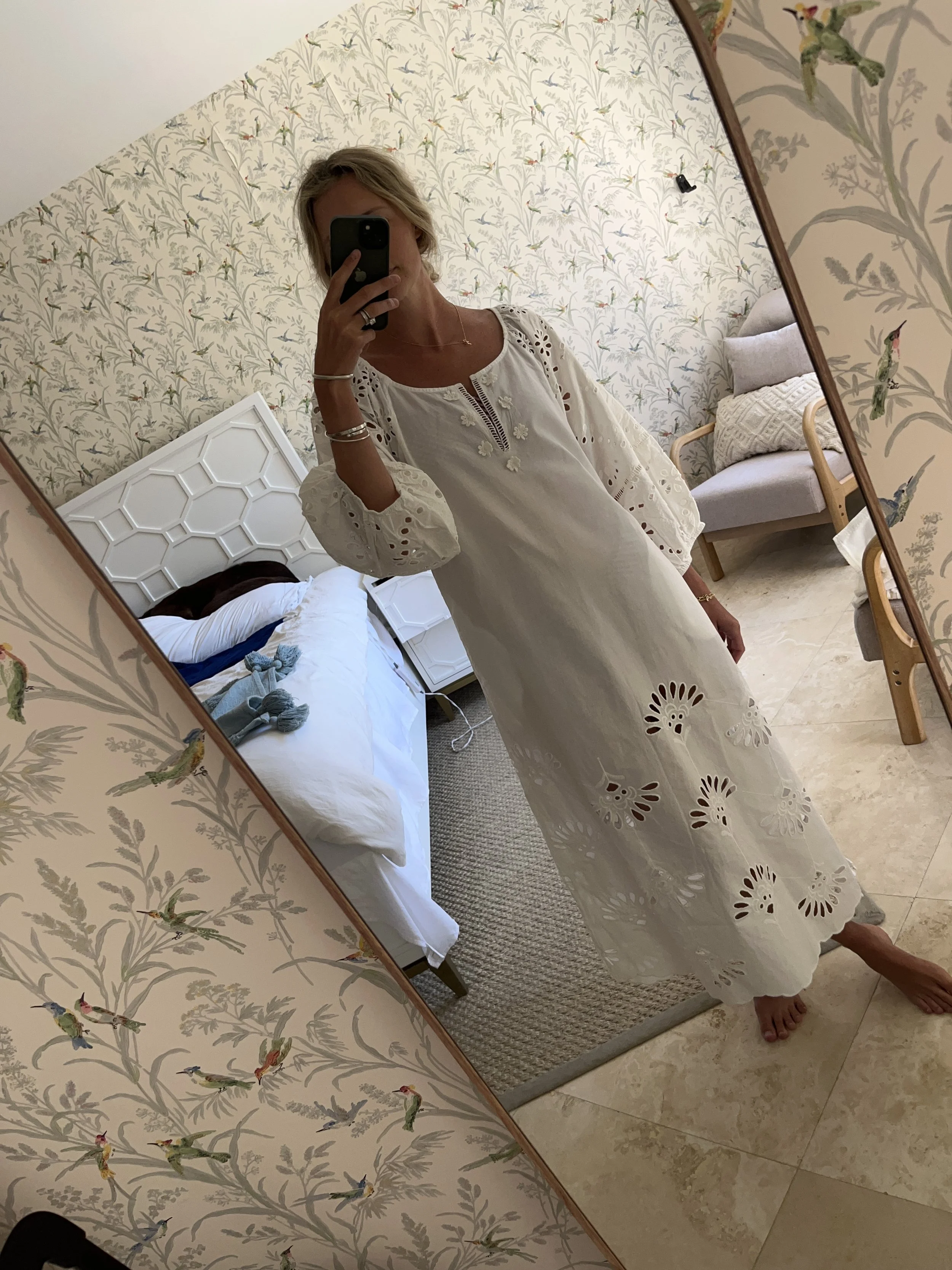 Person taking a mirror selfie in a room with wooden floors, wearing a striped brown and white long-sleeve shirt, light blue jeans, and black and white sneakers.