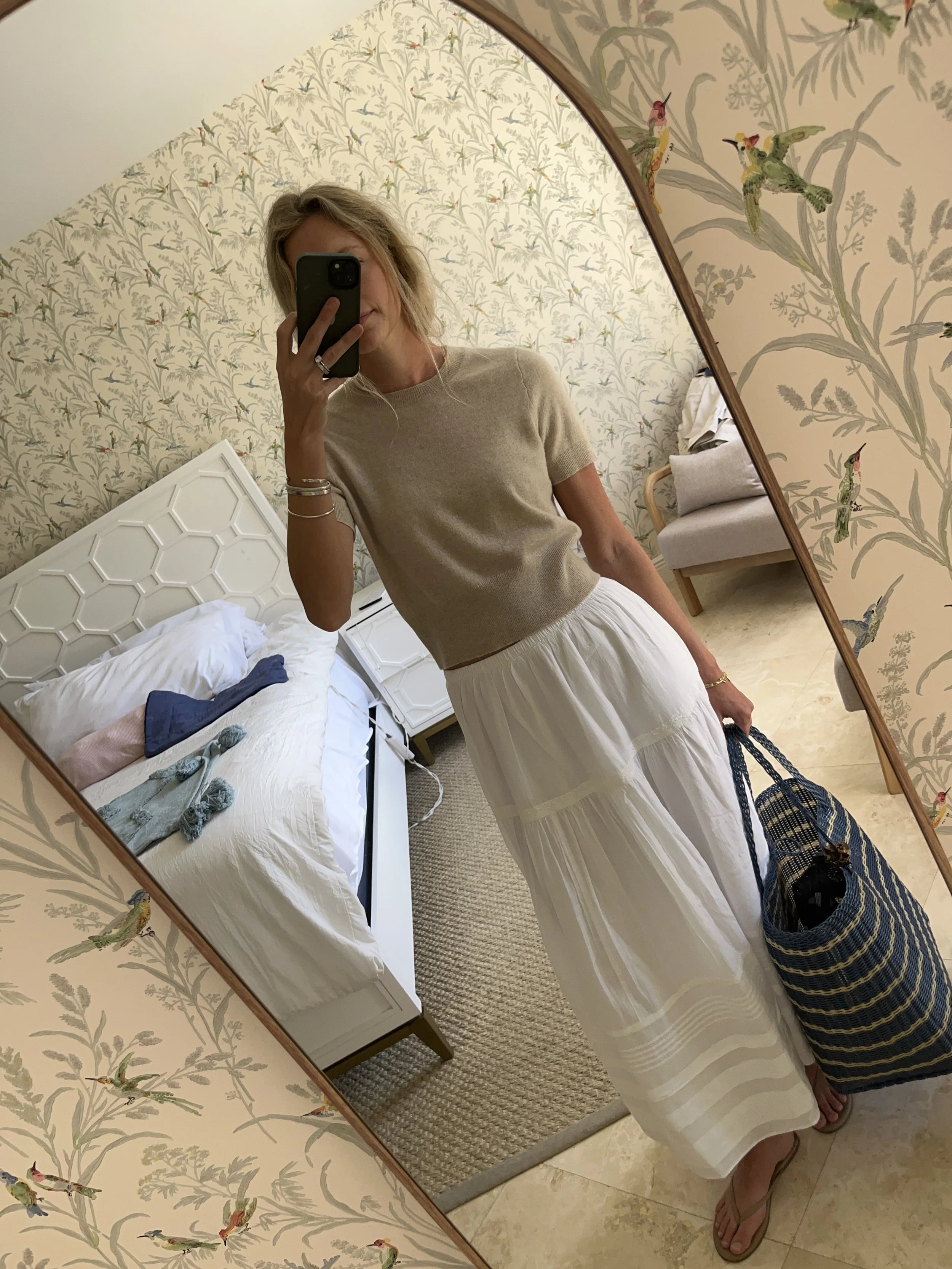 Person taking a mirror selfie in a room with wooden floors, wearing a striped brown and white long-sleeve shirt, light blue jeans, and black and white sneakers.