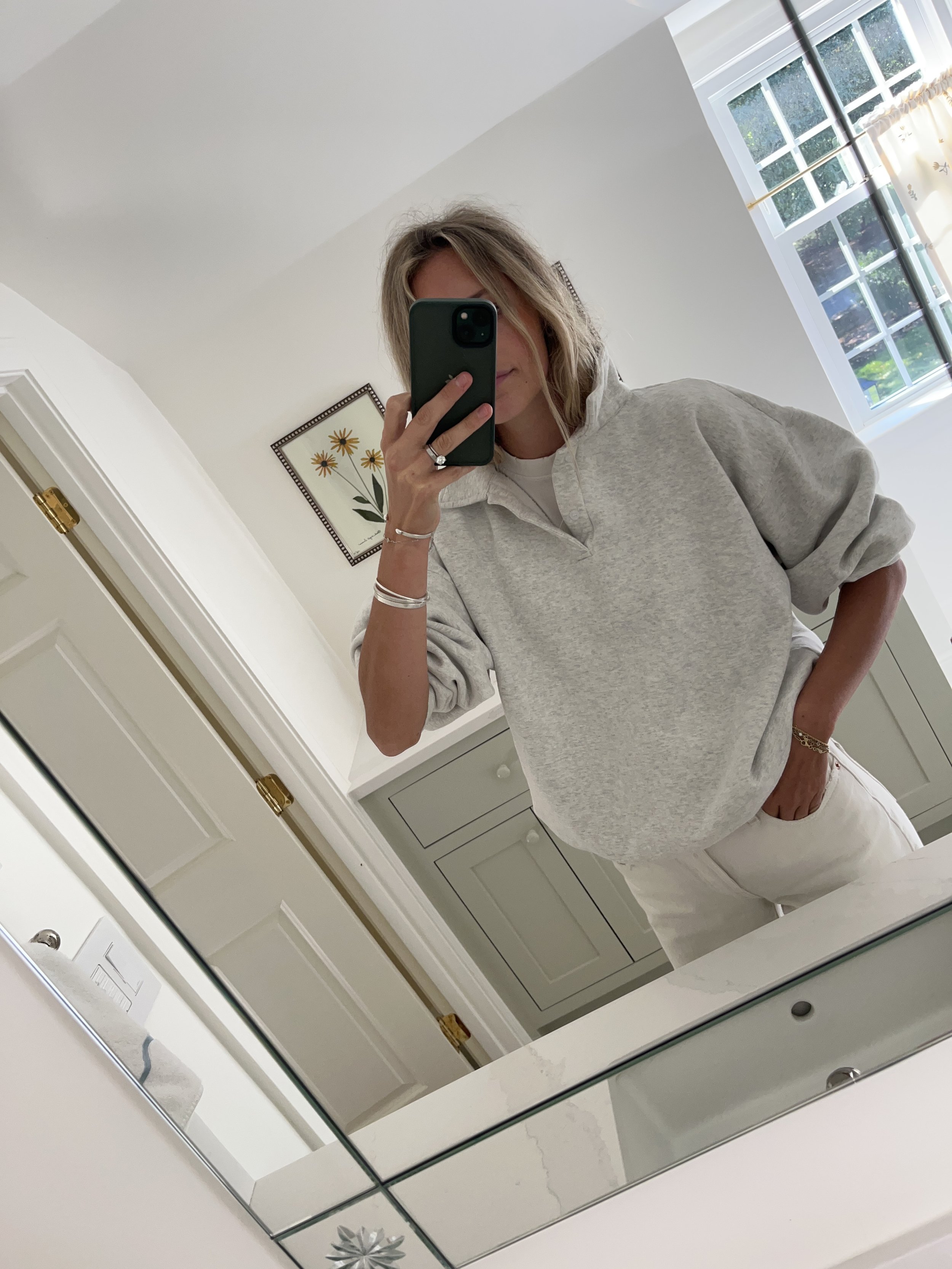 Person taking a mirror selfie in a room with wooden floors, wearing a striped brown and white long-sleeve shirt, light blue jeans, and black and white sneakers.