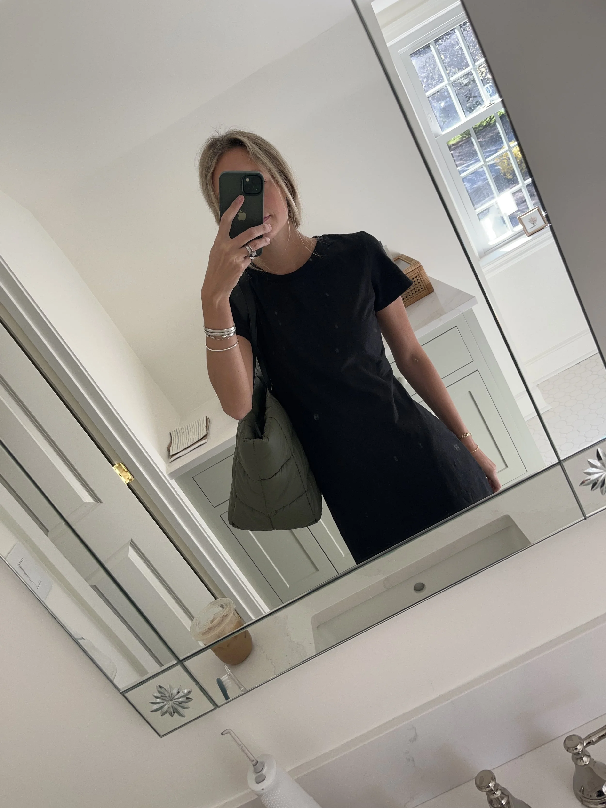 Person taking a mirror selfie in a room with wooden floors, wearing a striped brown and white long-sleeve shirt, light blue jeans, and black and white sneakers.