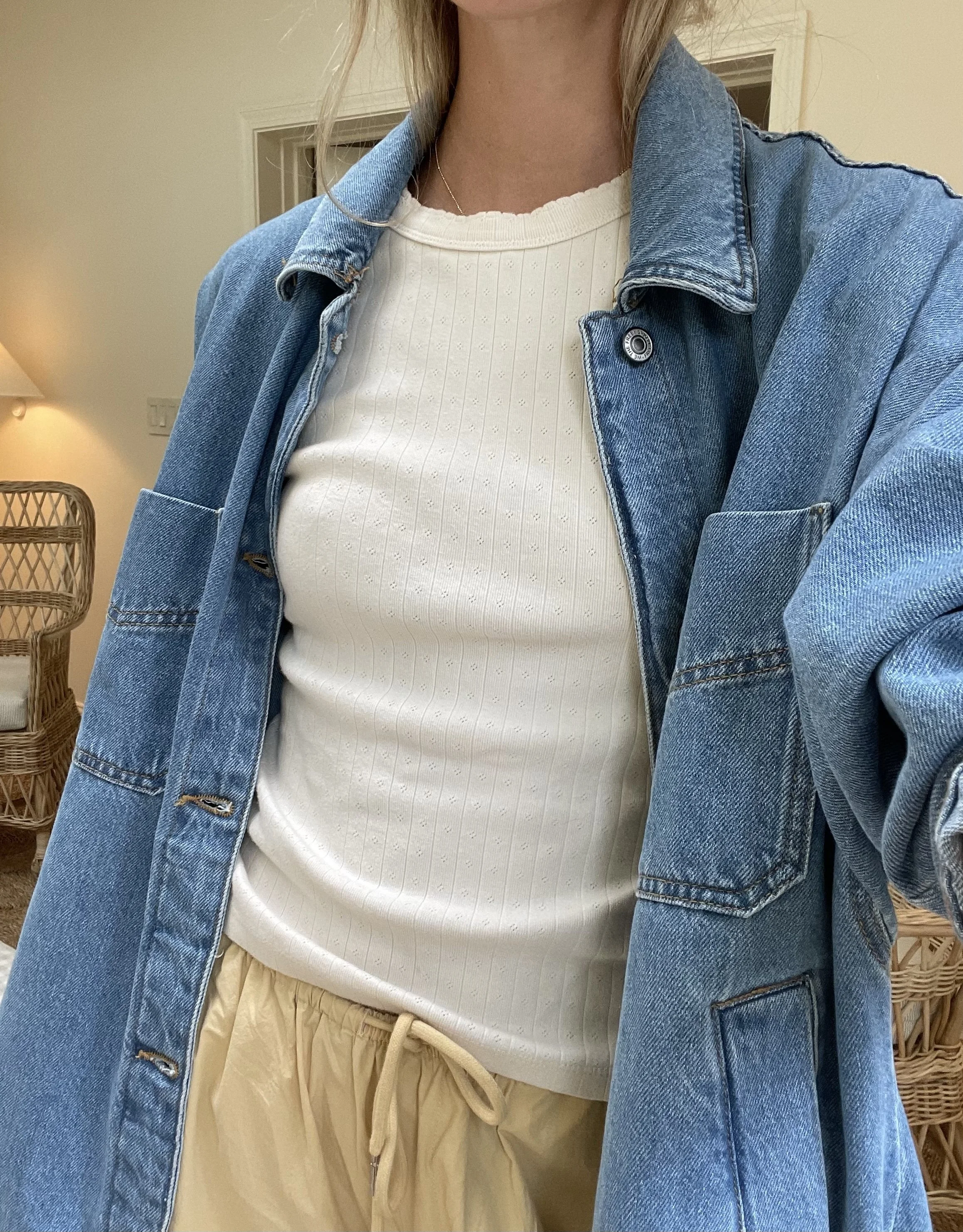 Person taking a mirror selfie in a room with wooden floors, wearing a striped brown and white long-sleeve shirt, light blue jeans, and black and white sneakers.