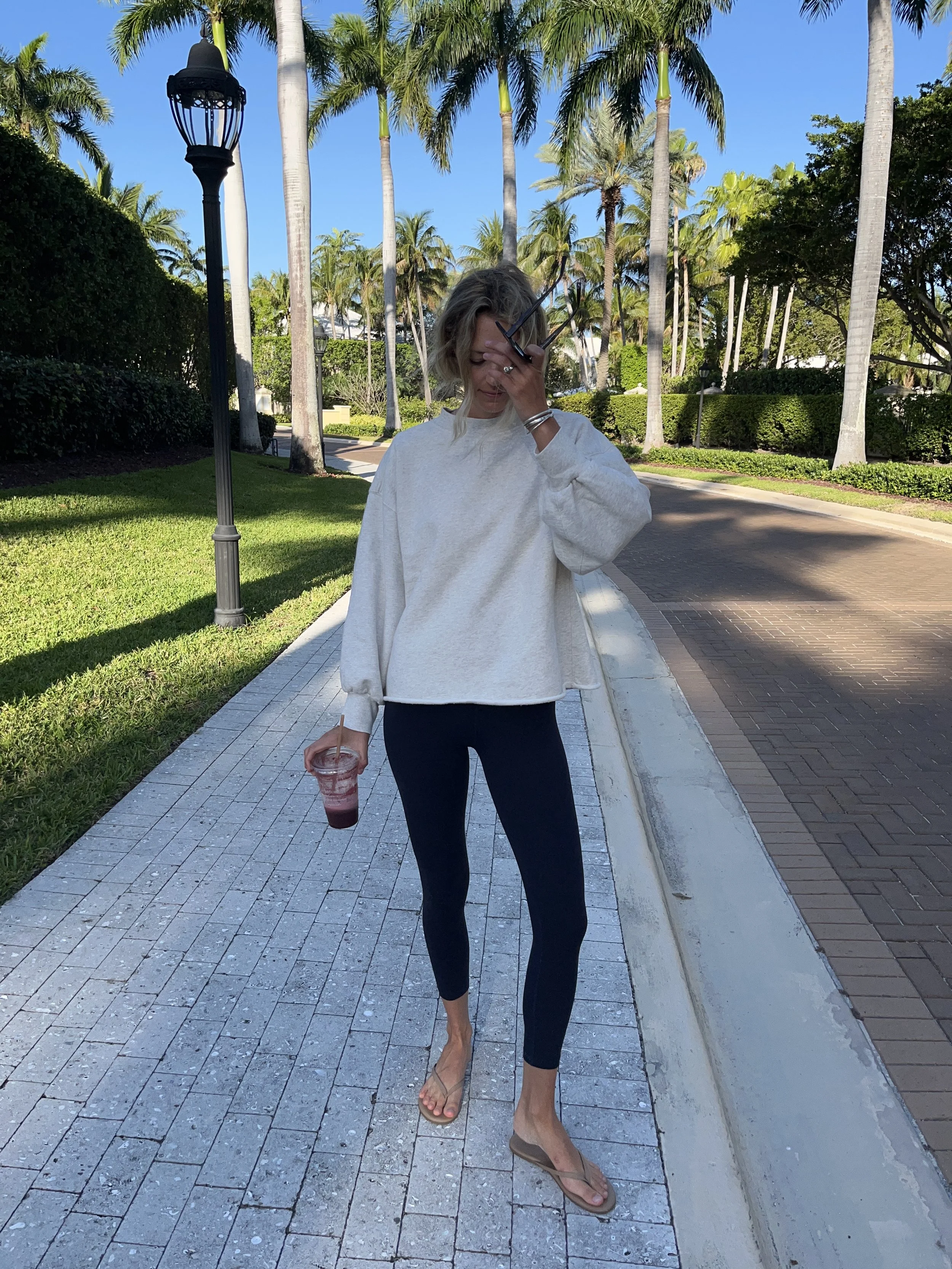 Person taking a mirror selfie in a room with wooden floors, wearing a striped brown and white long-sleeve shirt, light blue jeans, and black and white sneakers.