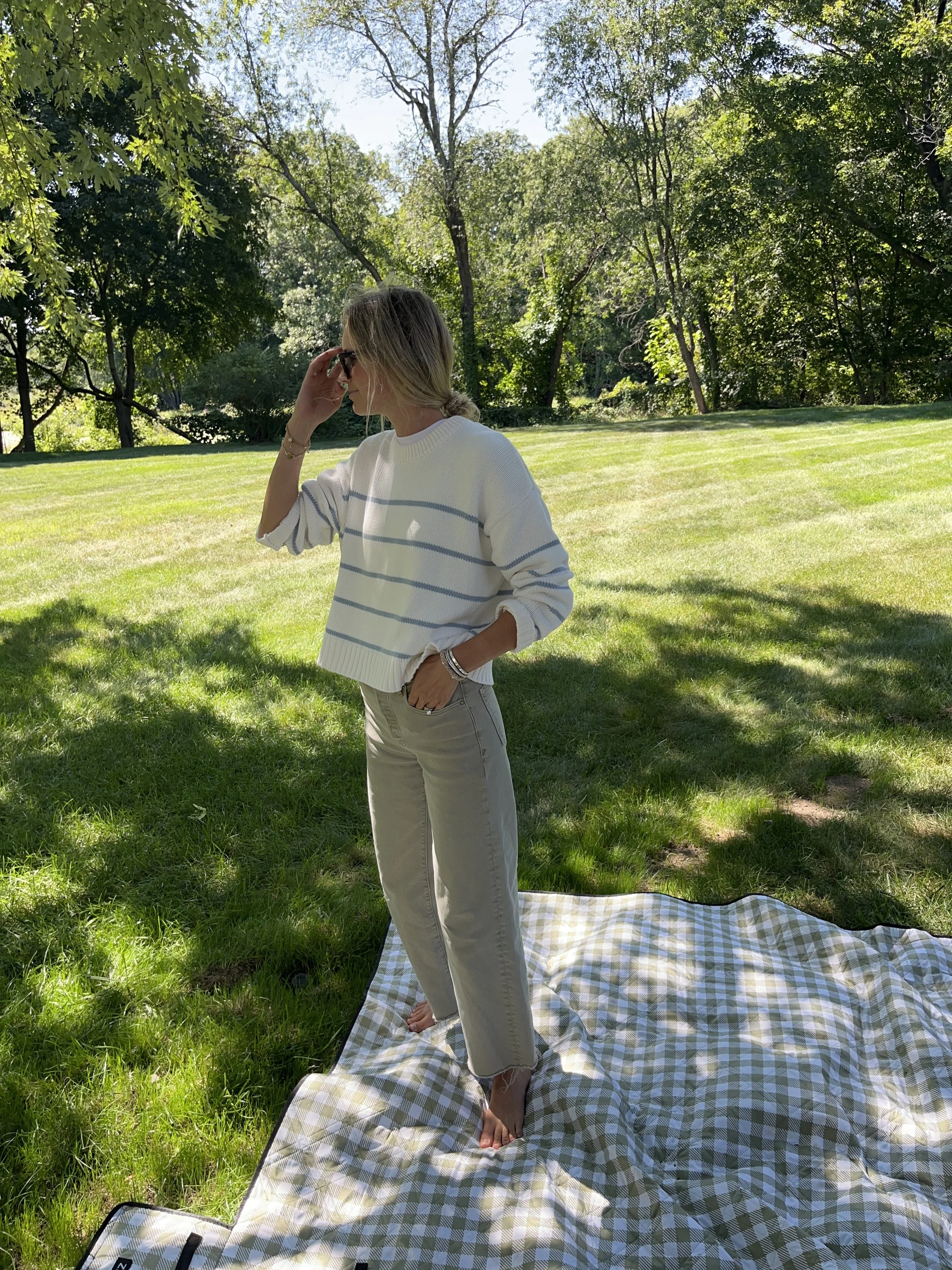 Person taking a mirror selfie in a room with wooden floors, wearing a striped brown and white long-sleeve shirt, light blue jeans, and black and white sneakers.